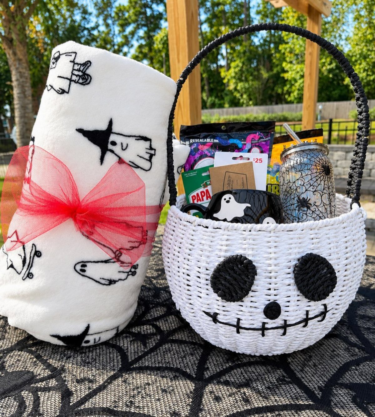 11 Gifts for Halloween Lovers: Candles, Socks and More 2 Jack Skellington woven basket filled with treats next to a ghost-patterned blanket.