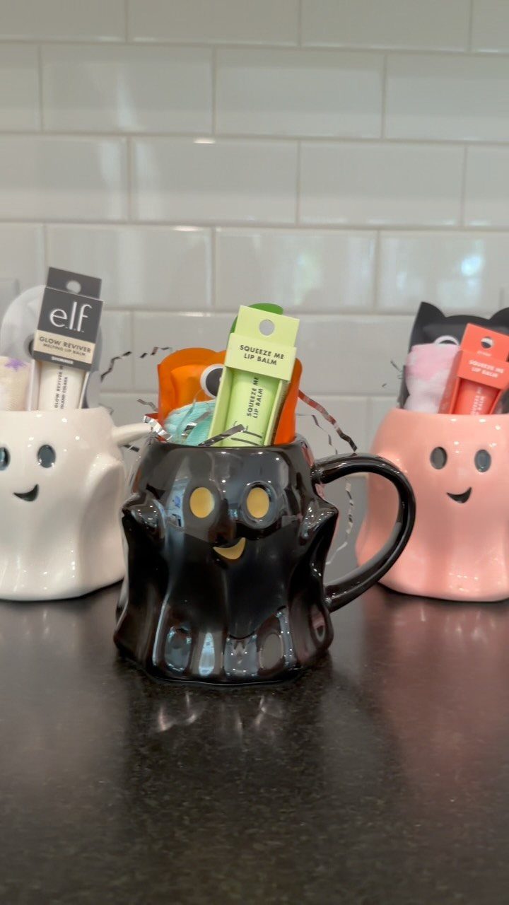 11 Gifts for Halloween Lovers: Candles, Socks and More 8 Three ghost-shaped ceramic mugs filled with small gifts on a dark kitchen counter.