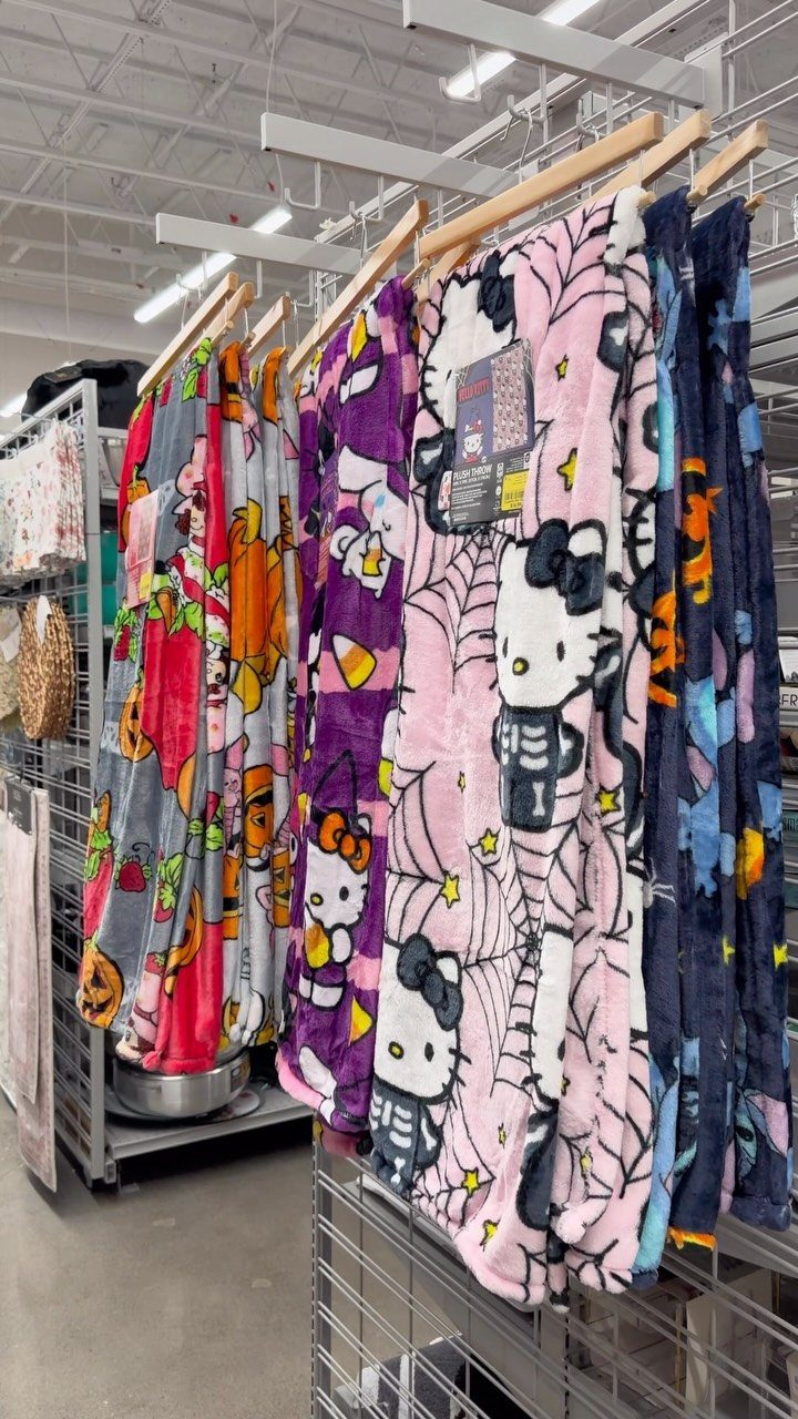 11 Gifts for Halloween Lovers: Candles, Socks and More 9 Halloween-themed Hello Kitty plush throw blankets hanging on a retail display rack.