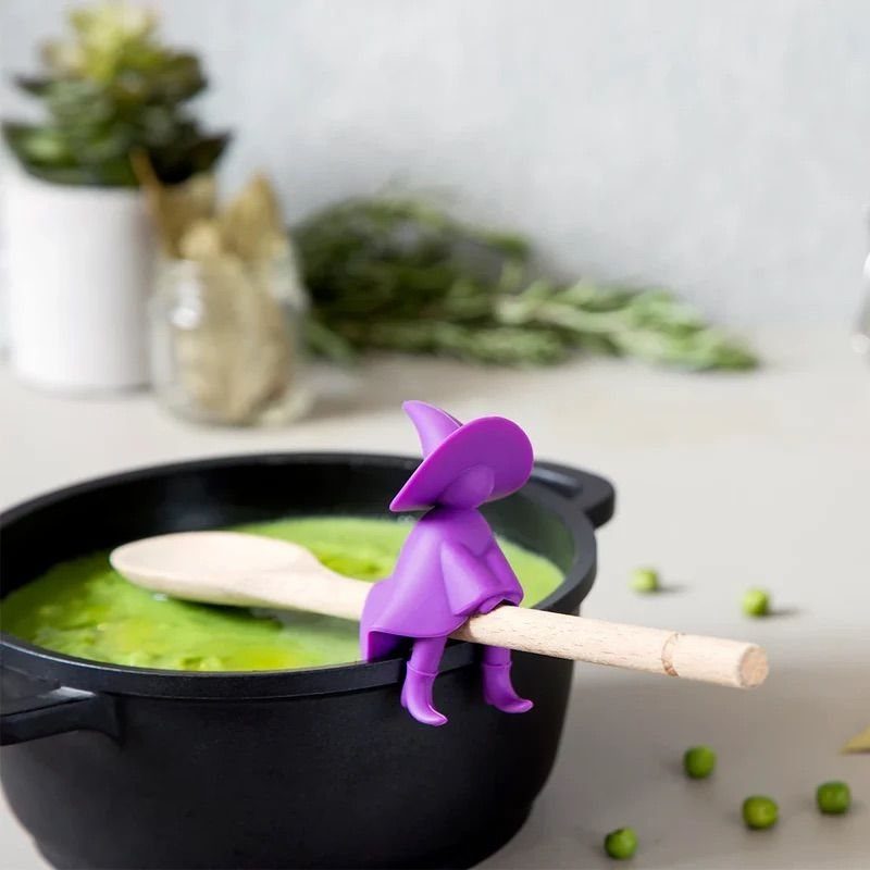 11 Gifts for Halloween Lovers: Candles, Socks and More 6 Purple witch silicone spoon rest holding a wooden spoon over green soup.
