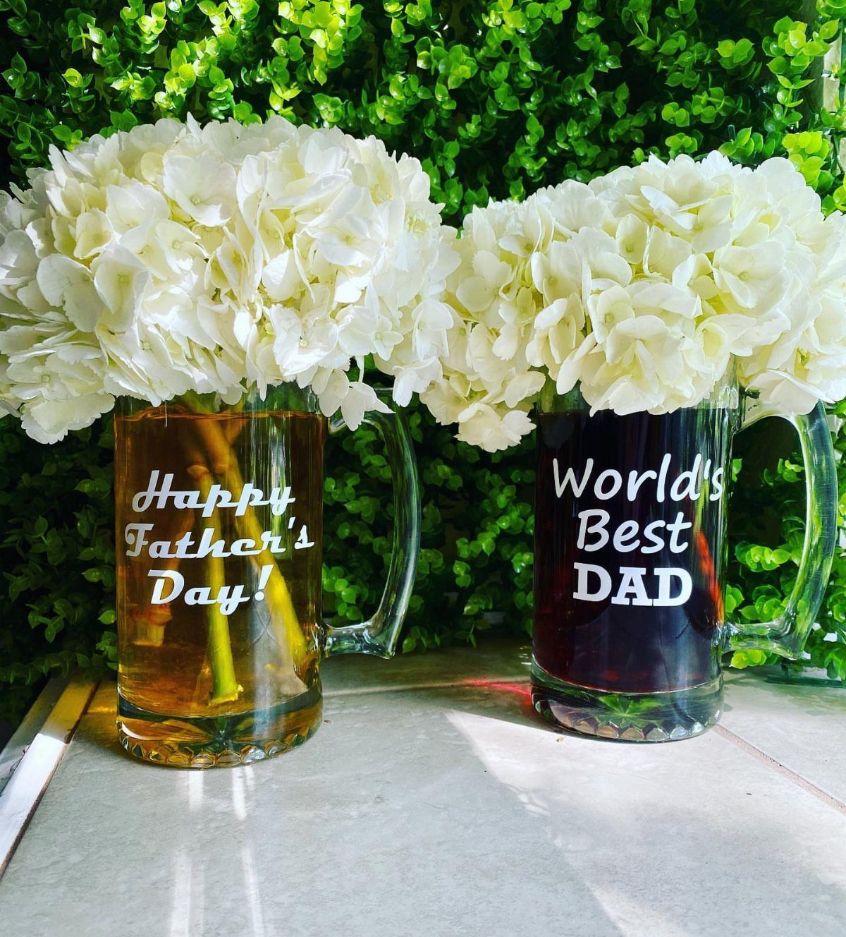 Two glass beer steins with Father's Day text holding white hydrangea flowers.