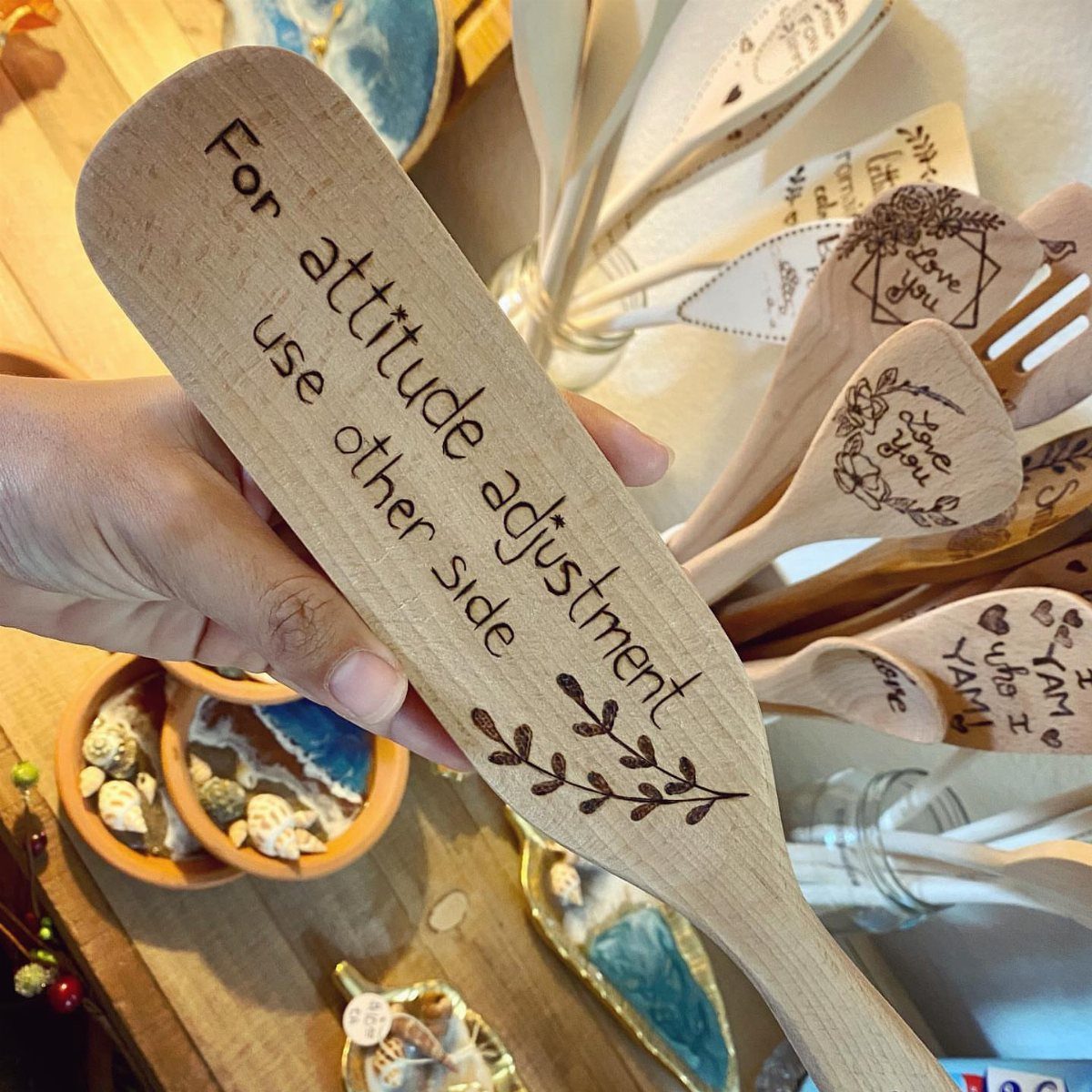Wooden spoon with engraved funny text about attitude adjustment held by a hand.