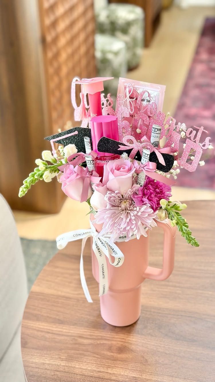 Graduation gift arrangement with pink flowers and cosmetics in a pink mug.