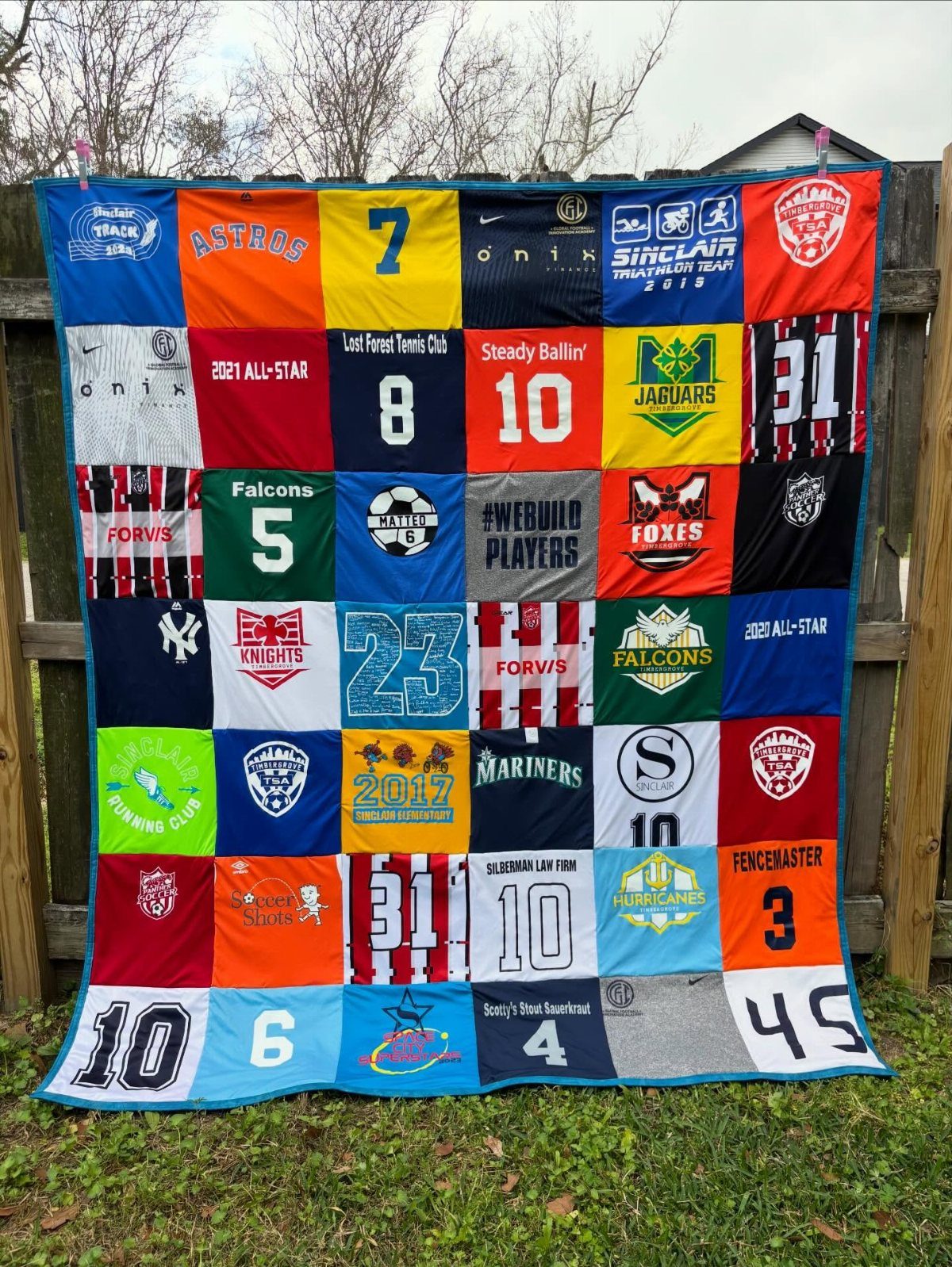 T-shirt quilt made from sports jerseys hanging against a wooden fence outdoors.