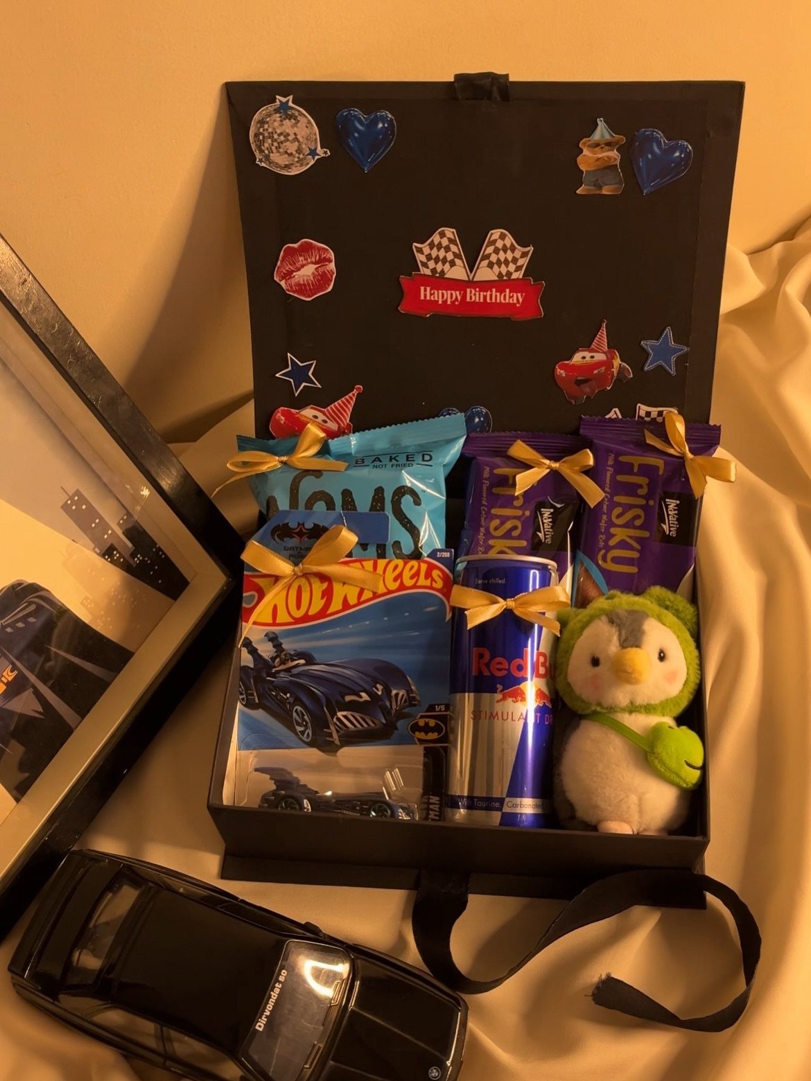 Birthday gift box for a guy containing toy cars, snacks, and a plush penguin.