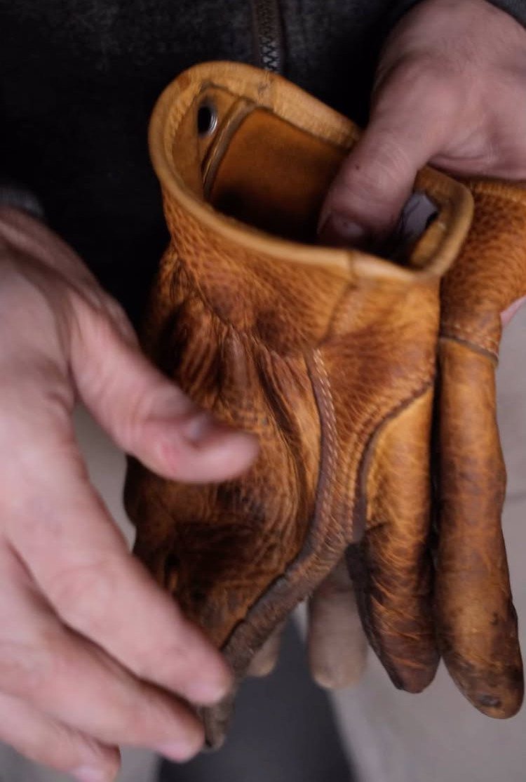 Brown leather work gloves held by a person's hands in a close-up shot.
