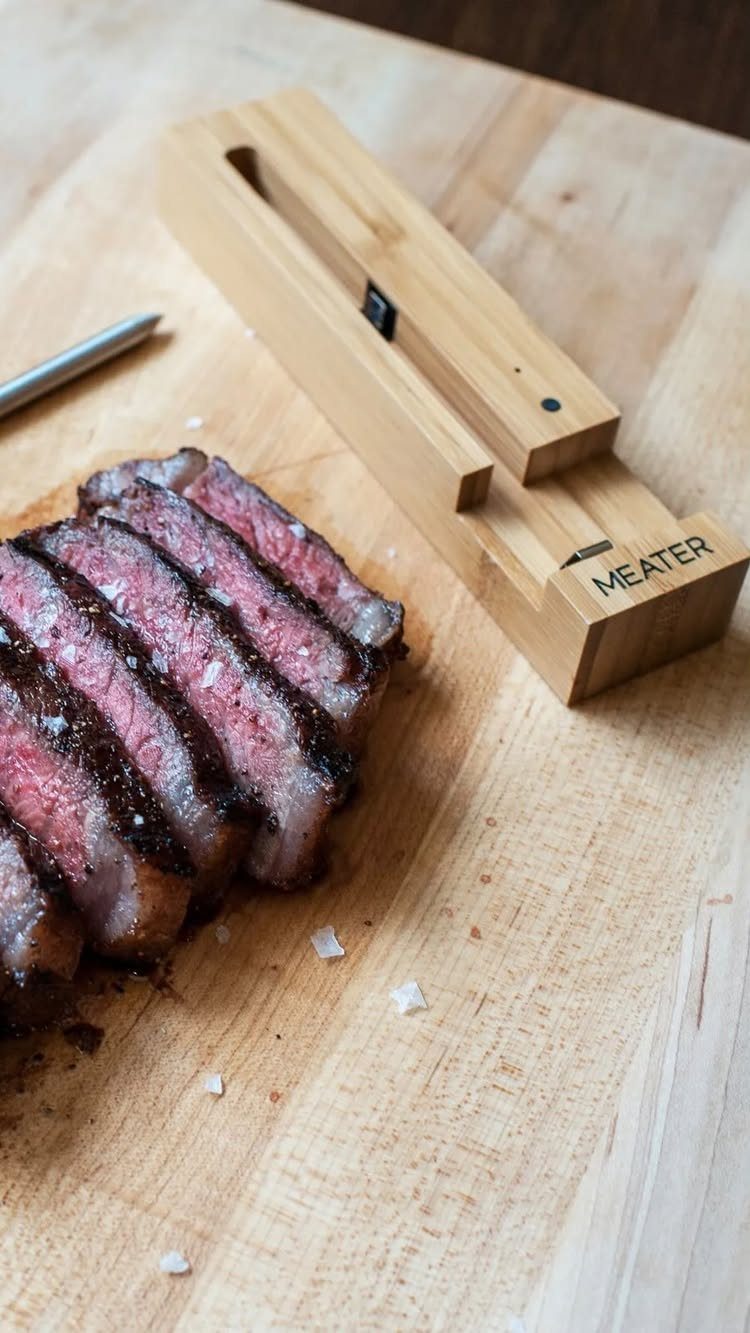 Slices of medium-rare steak next to a MEATER digital thermometer on wooden board