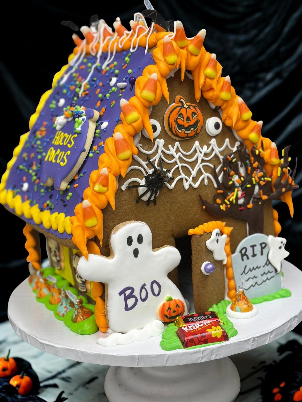 Haunted gingerbread house decorated with purple icing, candy corn, and a ghost cookie.