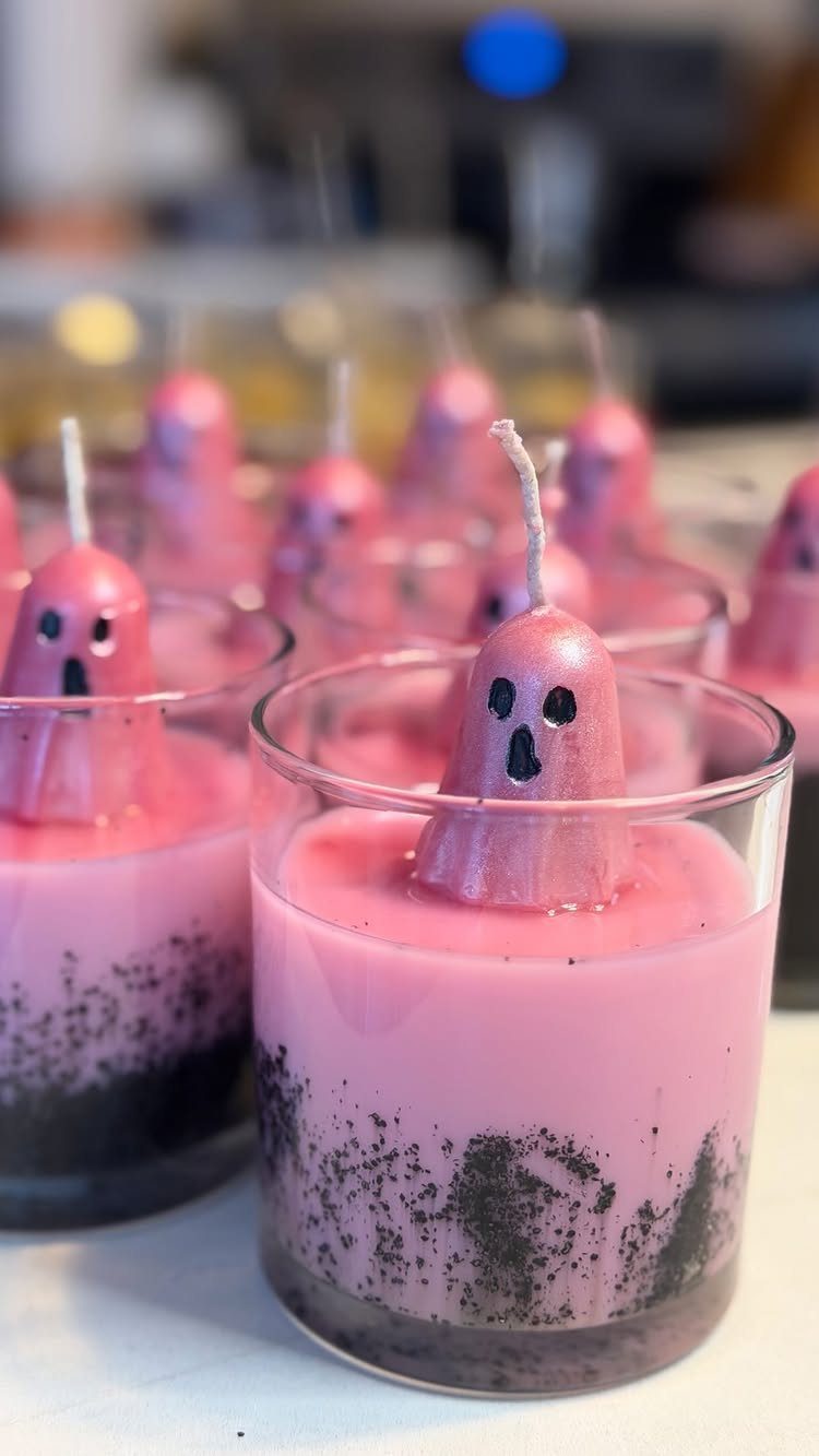Pink ghost-shaped candles in glass jars with dark grey wax bases.
