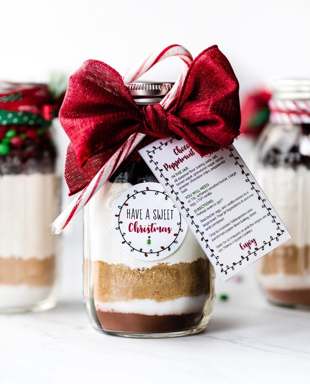 Layered cookie ingredients in a glass jar with a red bow and labels.
