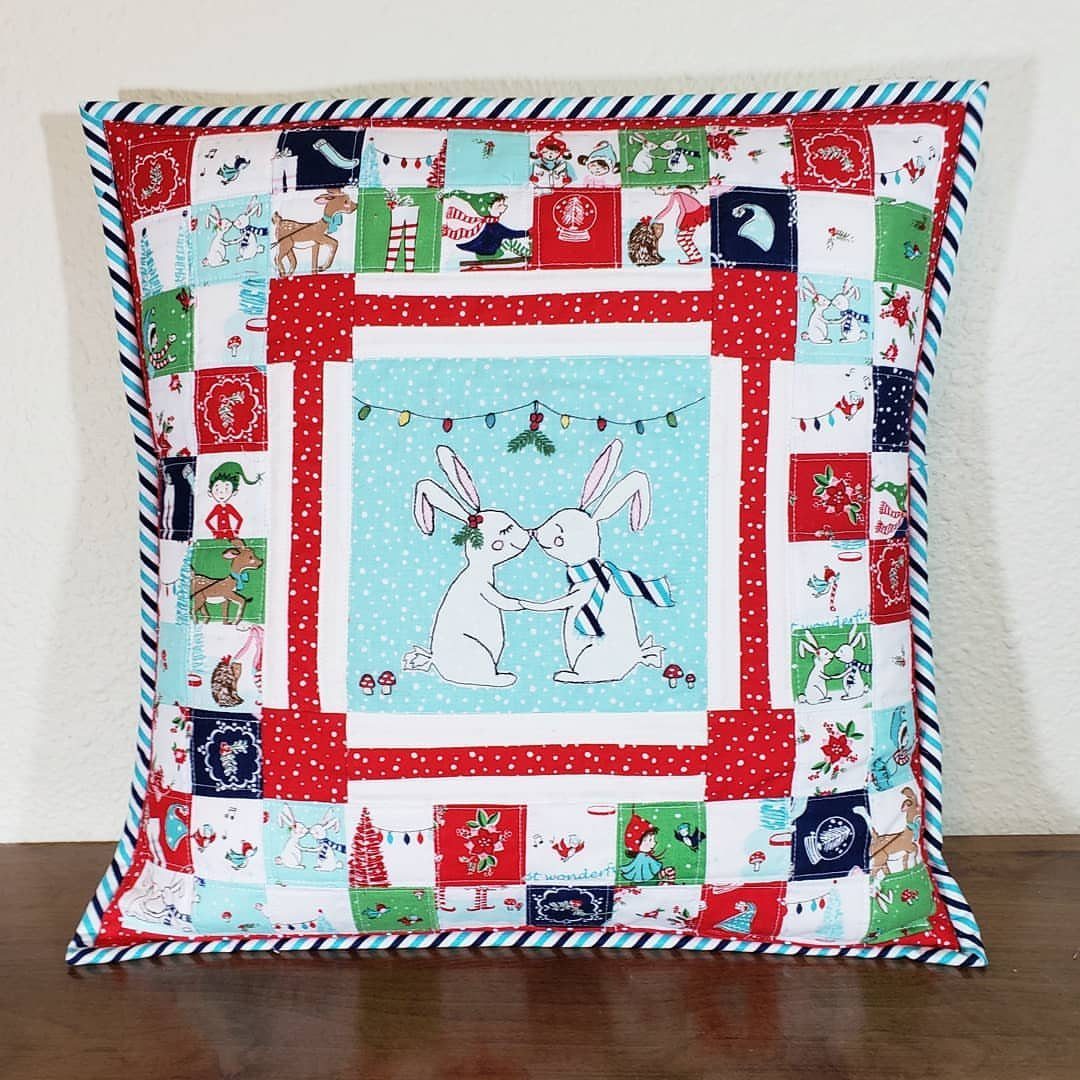 Patchwork holiday pillow featuring two white rabbits in the center and festive borders.