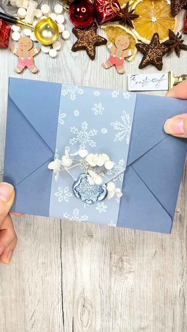 Blue envelope decorated with white dried flowers and a heart charm on wood.
