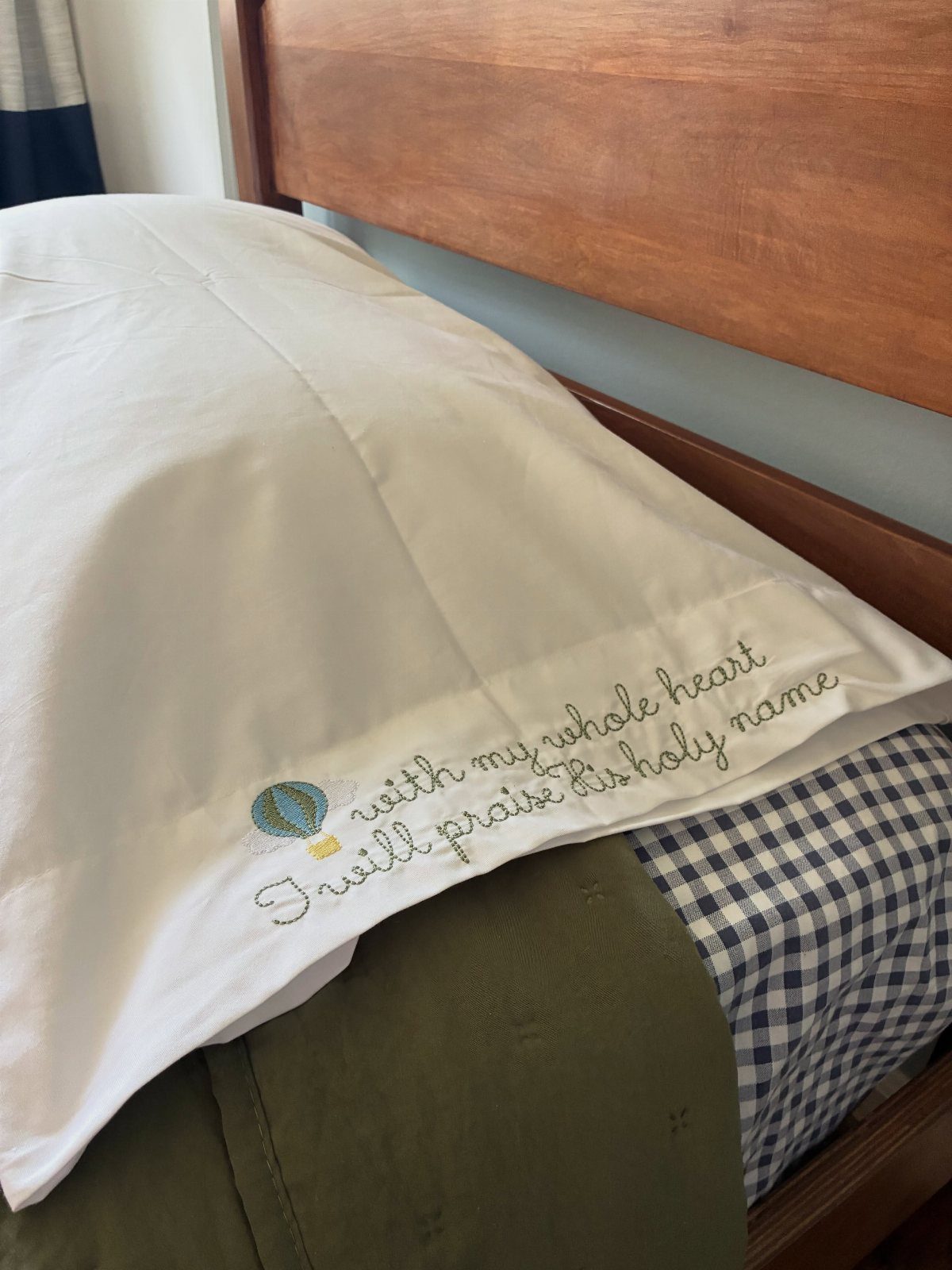 White pillowcase with embroidered cursive text and a small hot air balloon icon.