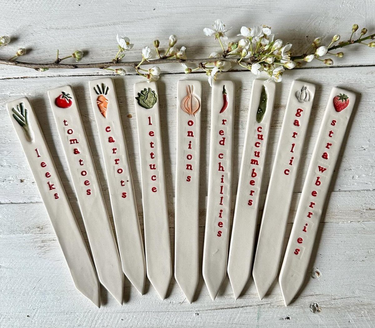 White ceramic garden markers with painted vegetables and red text on white wood.