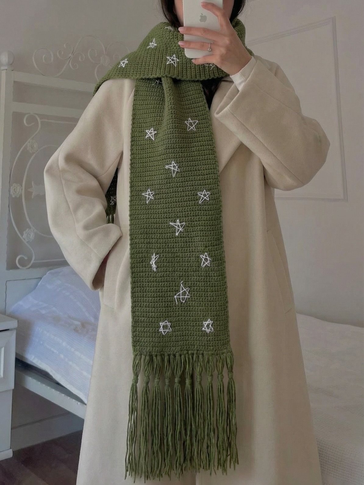 Olive green knitted scarf with white stars worn with a cream coat.
