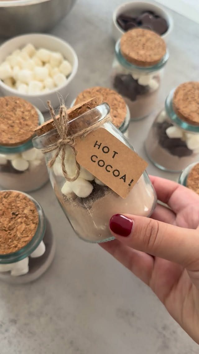 Hand holding a small glass jar of layered hot cocoa mix with marshmallows.