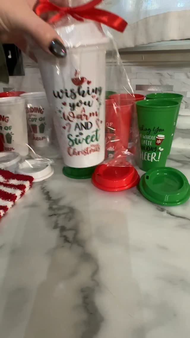 14 Holiday Christmas Gifts for Kids, Couples and Coworkers 5 Festive travel mugs wrapped in plastic with ribbons on a marble countertop.