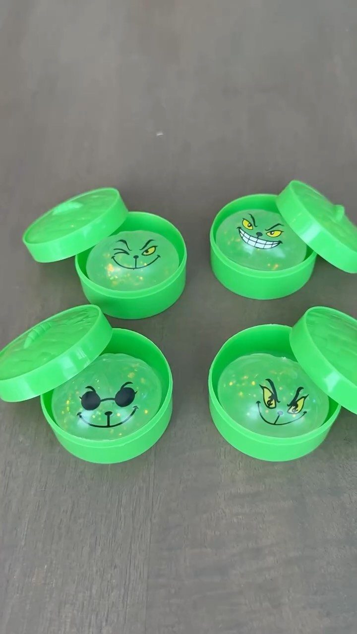 14 Holiday Christmas Gifts for Kids, Couples and Coworkers 9 Four green containers of Grinch-themed glitter slime on a grey wooden surface.