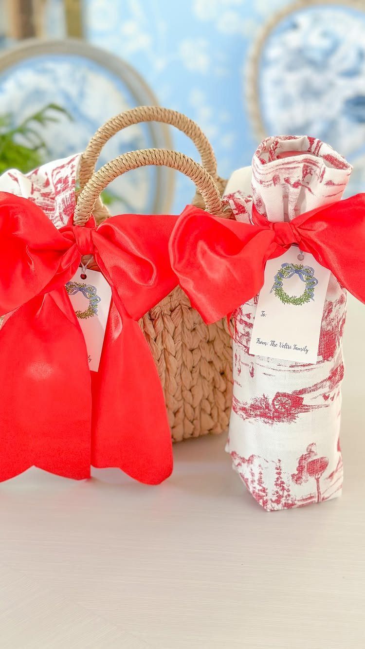 Woven gift basket and wrapped bottle with large red satin bows and tags.