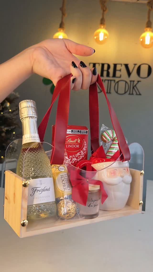 Holiday gift tray with sparkling wine, chocolates, and a Santa mug held by ribbons