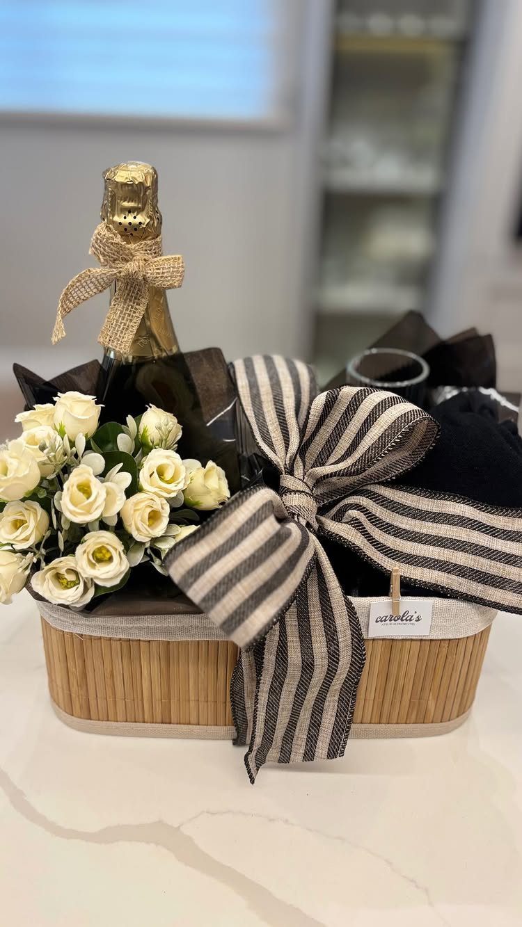Gift basket with sparkling wine, white roses, and a large striped ribbon bow.