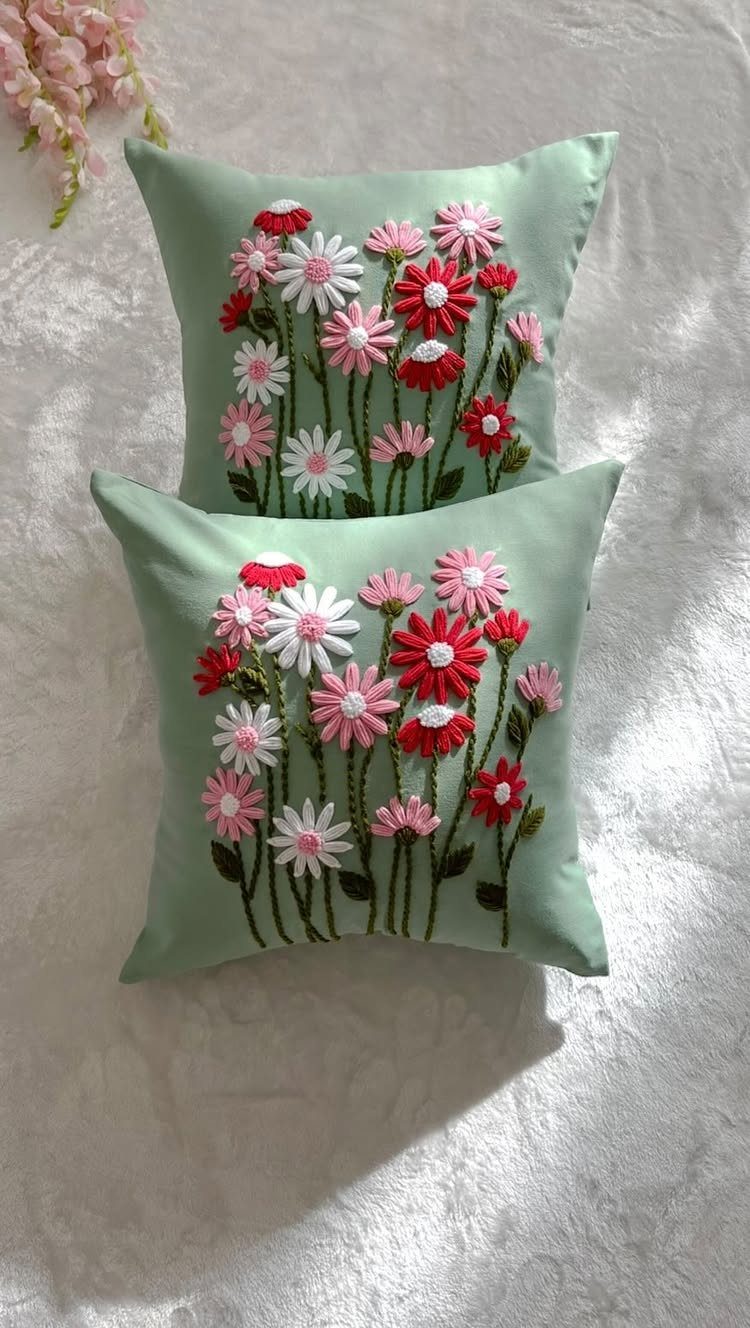 Two light green pillows with embroidered red and white daisy floral patterns.