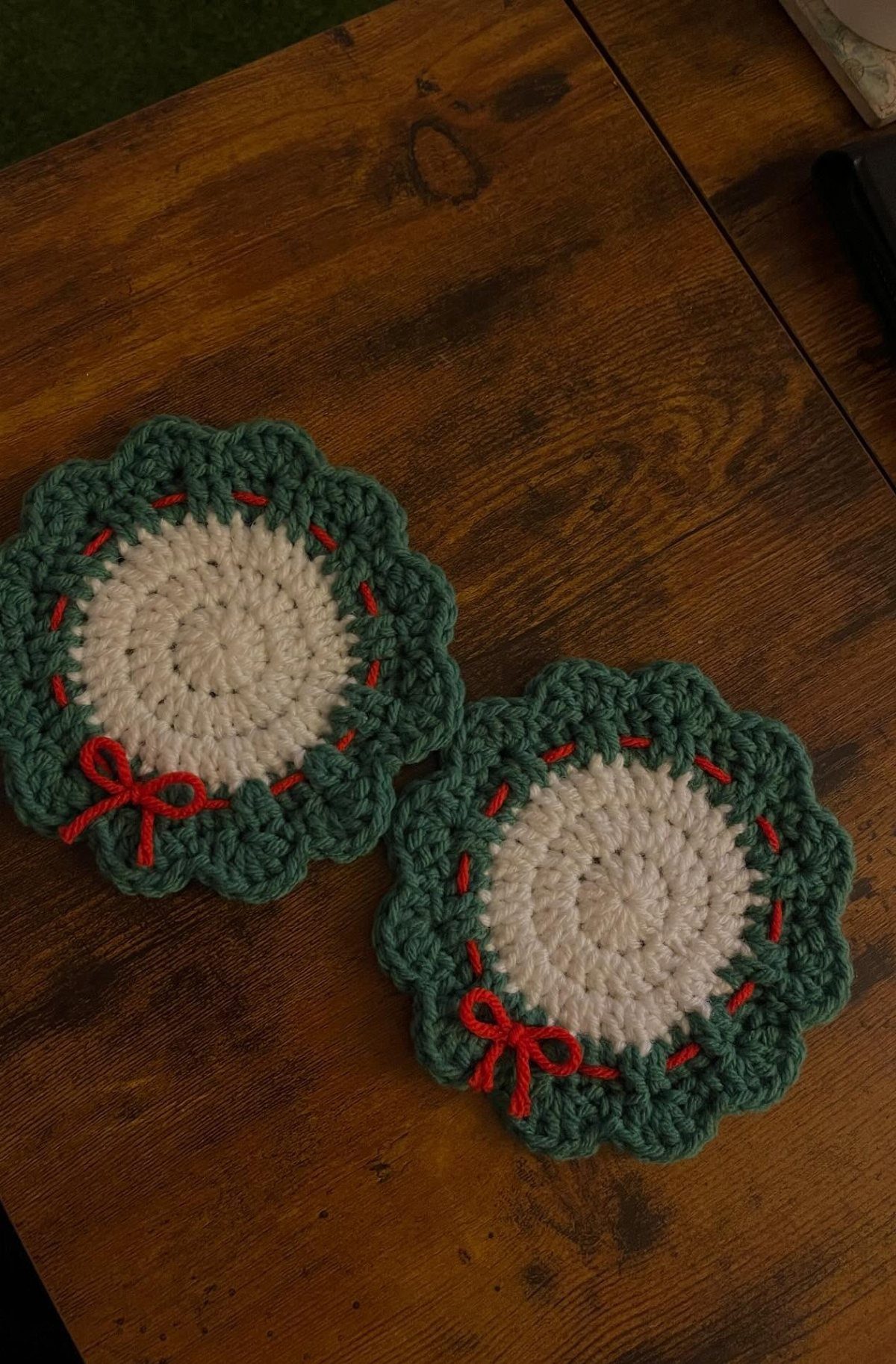 Crocheted wreath coasters with white centers and red bows on a wooden table.