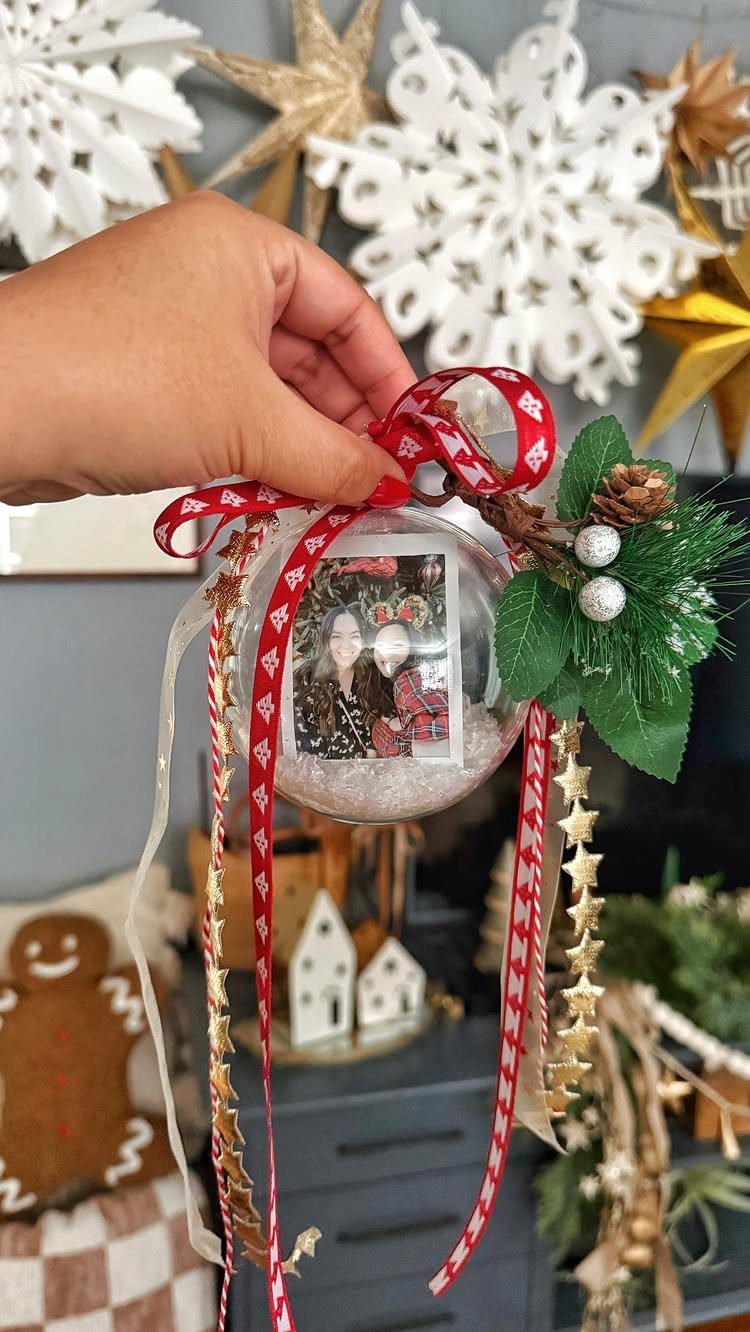 Clear glass Christmas ornament containing a small photo, decorated with red ribbons and greenery.