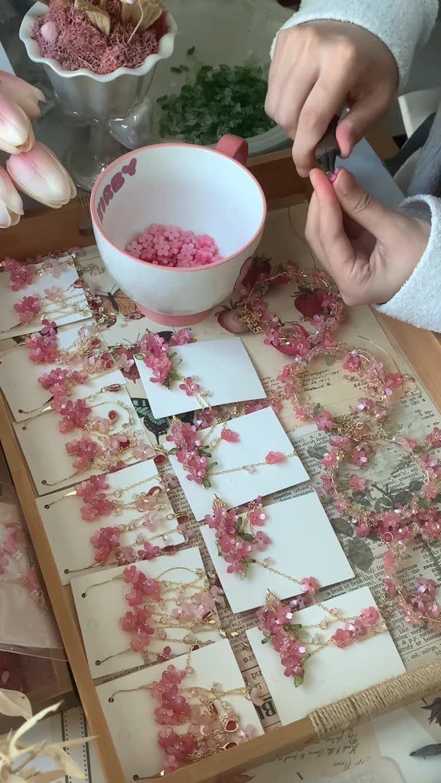 Hands assembling pink beaded jewelry on a wooden tray with finished bracelets.