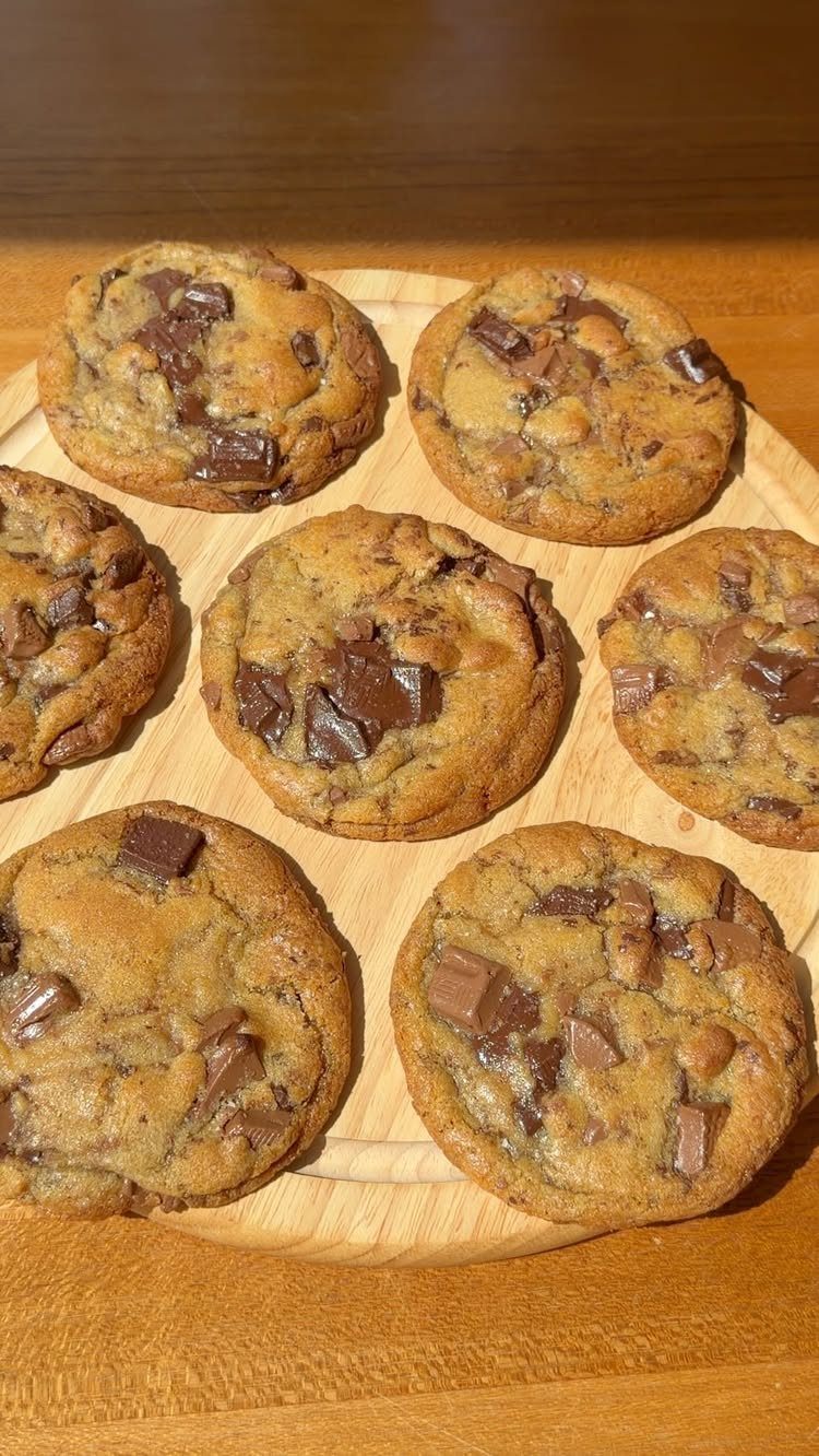 Chocolate chip cookies with large chocolate chunks on a light wooden platter.