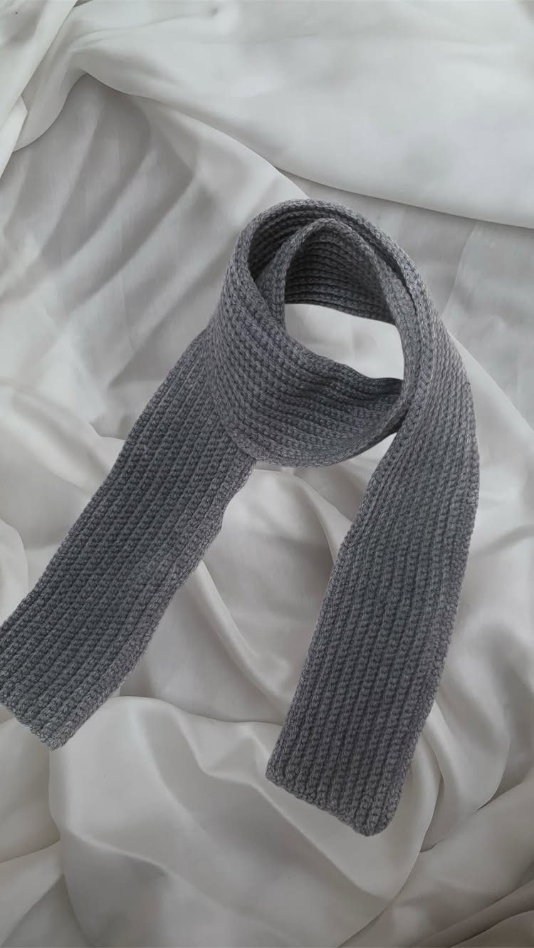 Grey ribbed knitted scarf draped over a white fabric background.