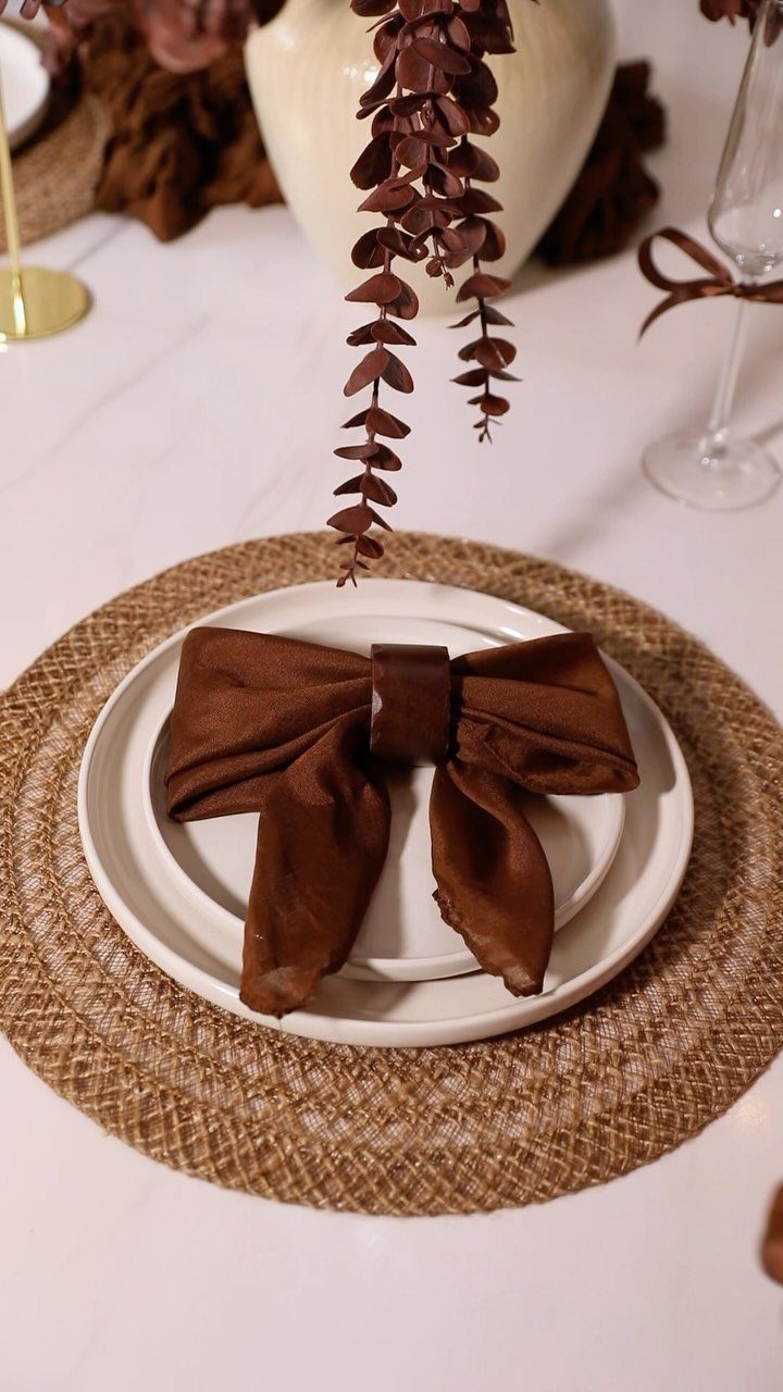 Brown fabric napkin folded as a bow tie on a white dinner plate