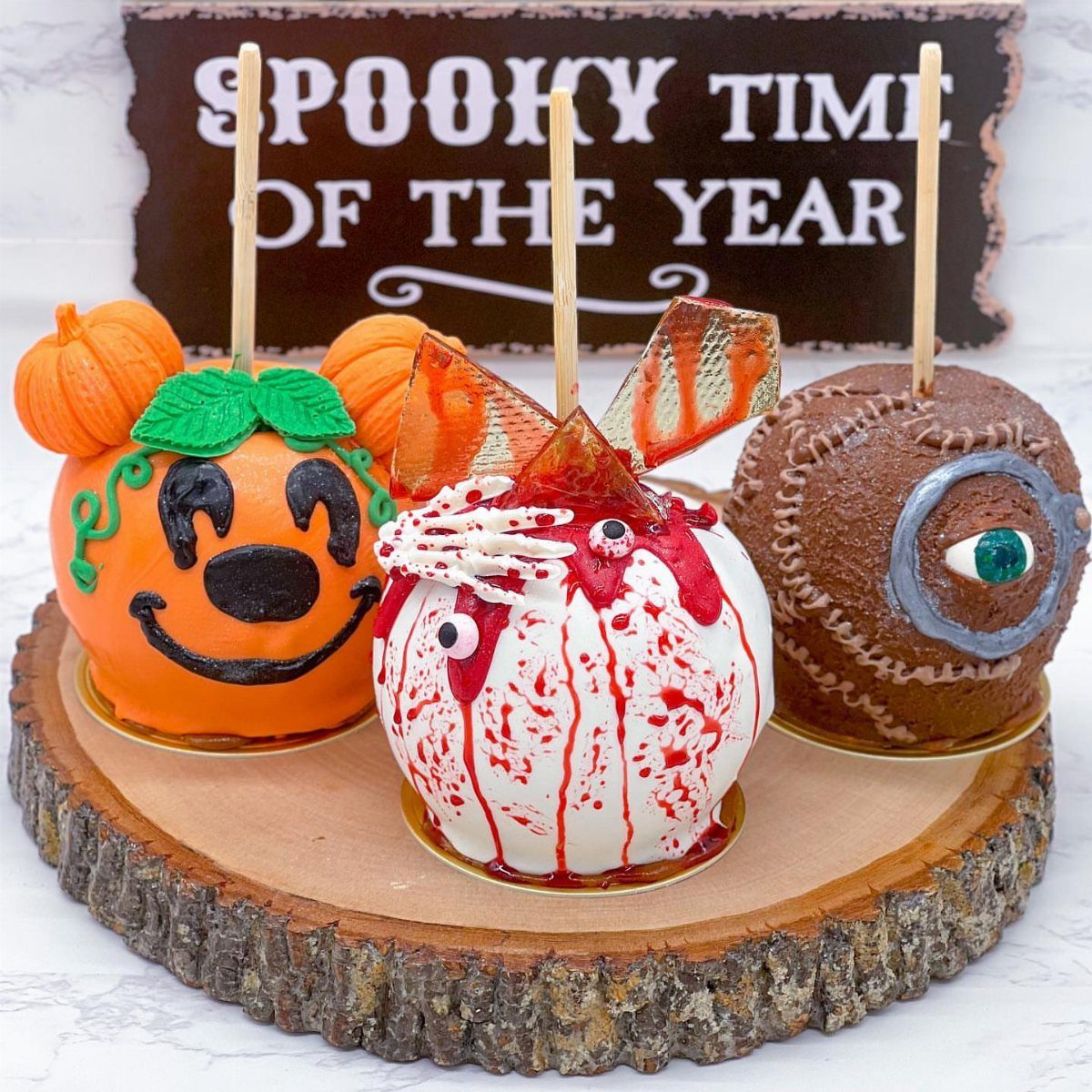 Three decorated Halloween candy apples on a rustic wooden slice platter.