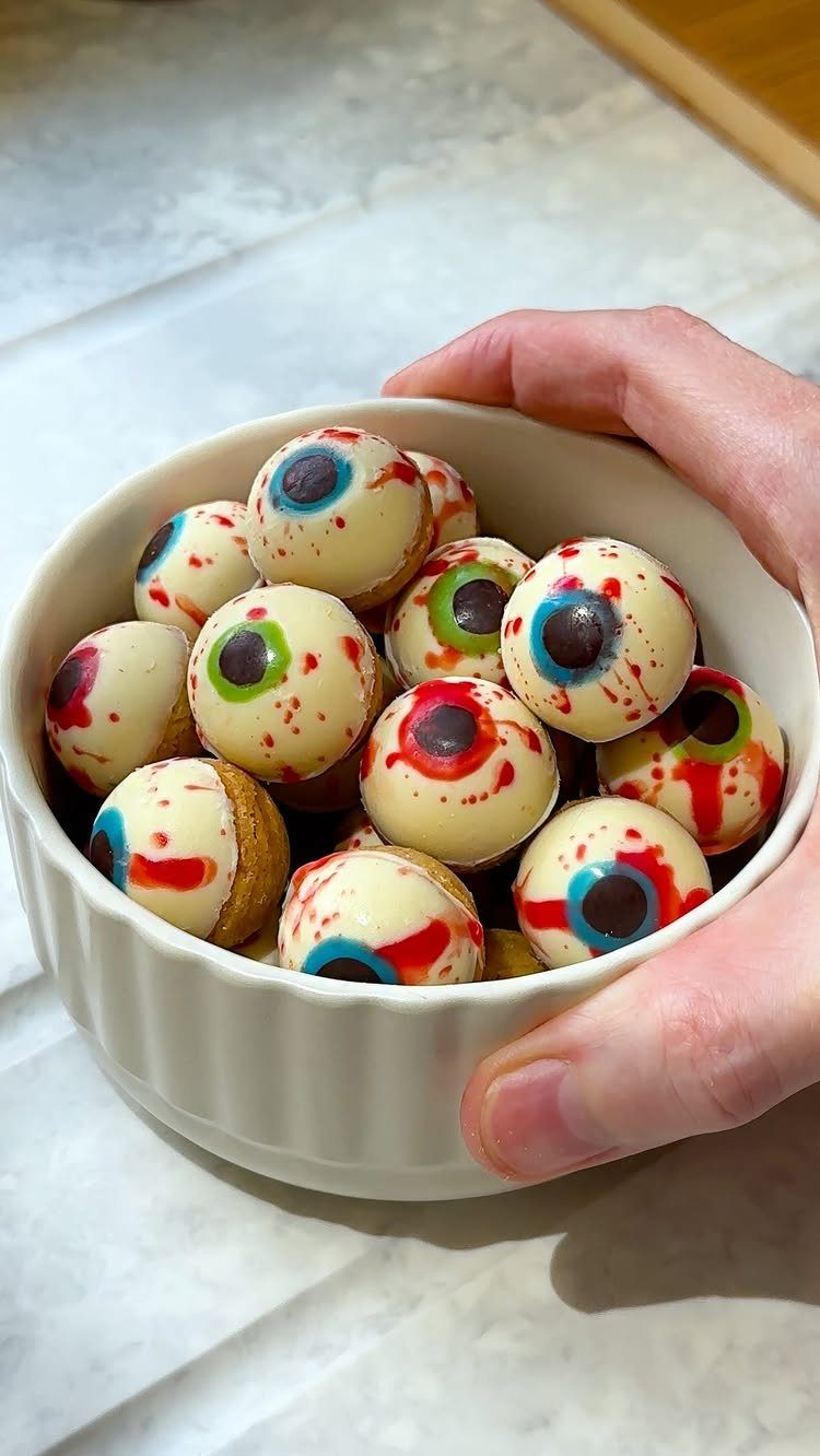 Eyeball-shaped cookies with colorful irises and red veins in a white bowl.