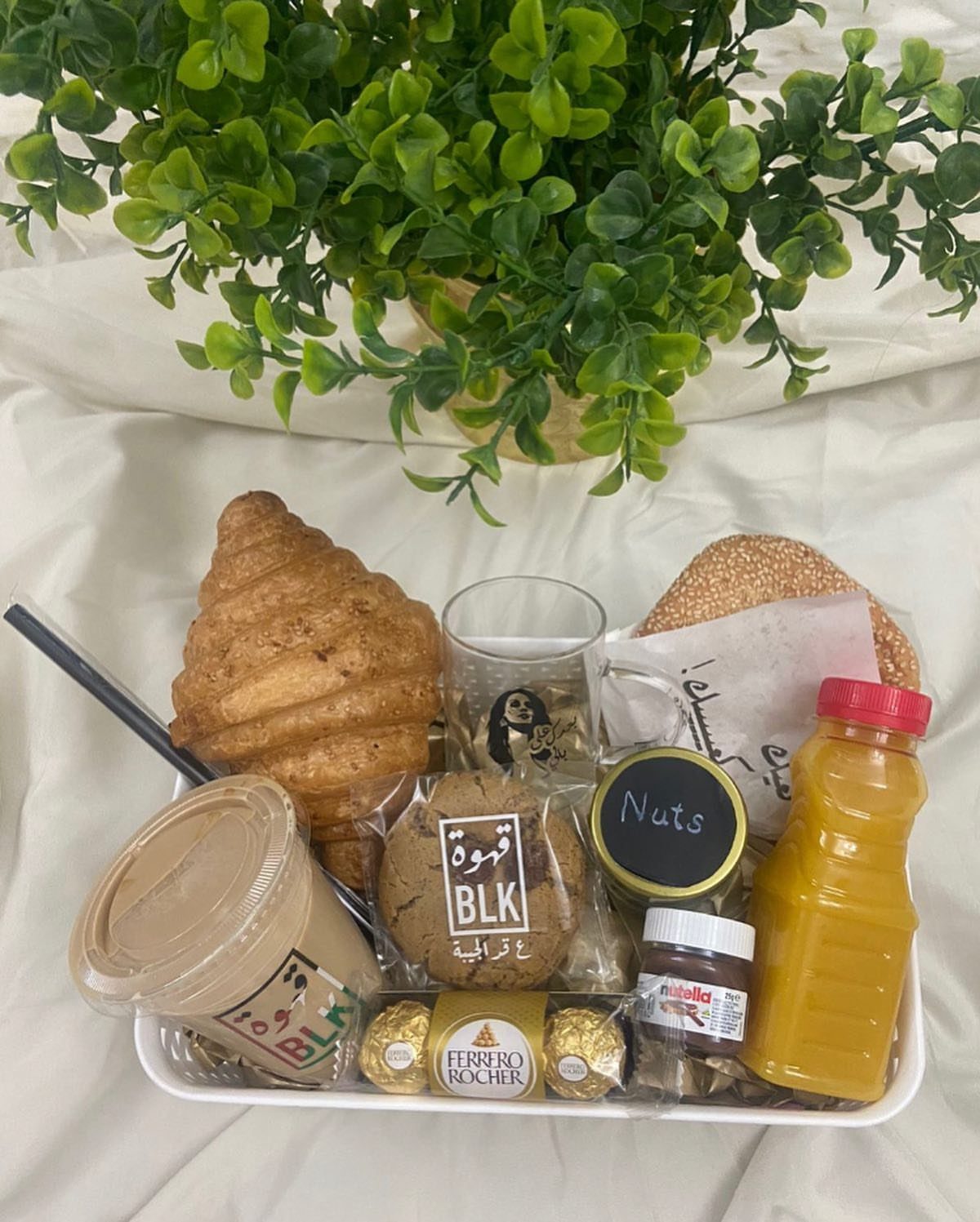 14 Household Gift Basket Ideas for Every Occasion 13 Breakfast gift tray with croissant, orange juice, coffee, and sweets near a green plant.