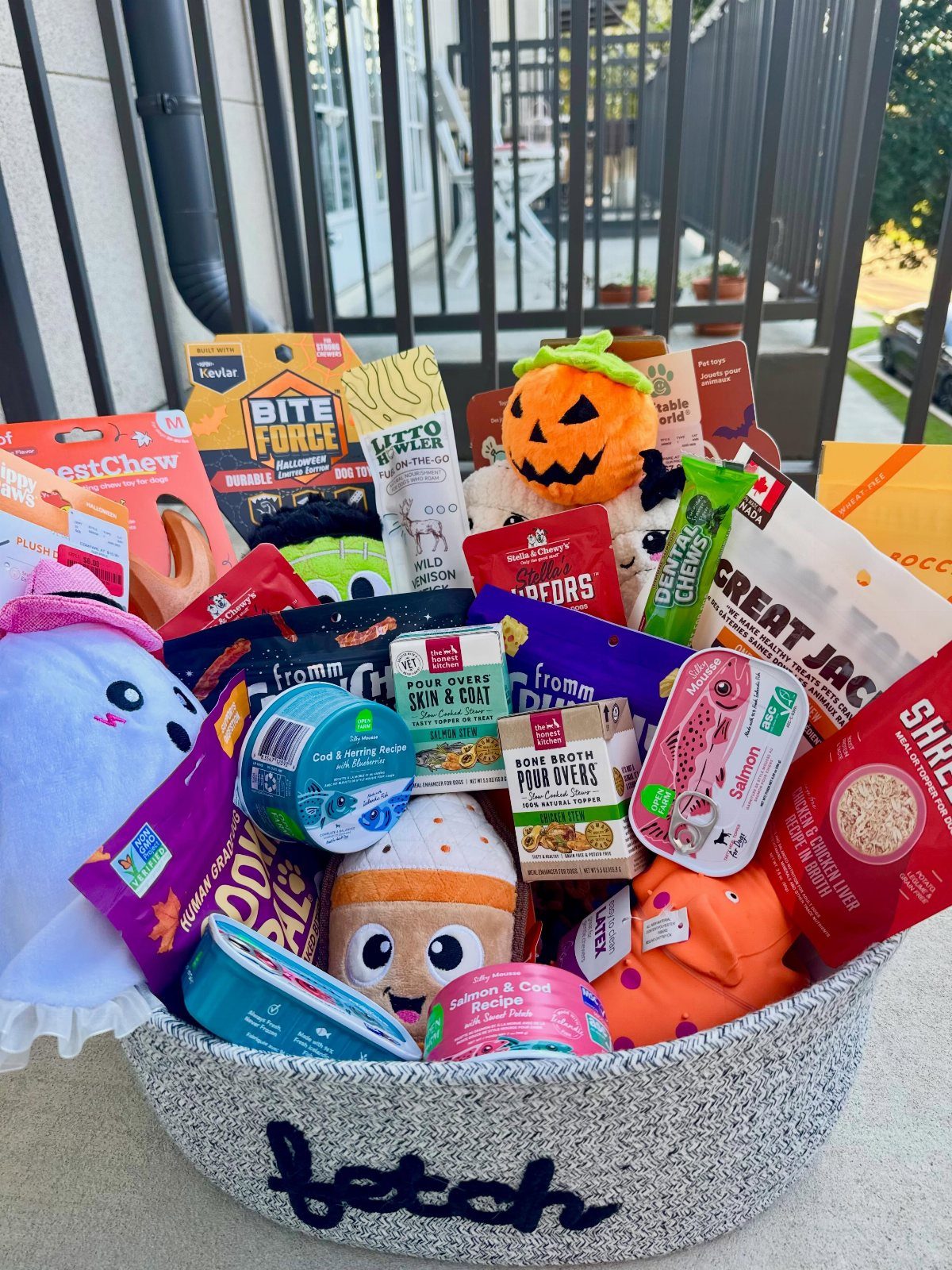 14 Household Gift Basket Ideas for Every Occasion 10 Dog gift basket filled with treats, toys, and pet supplies in a grey basket.