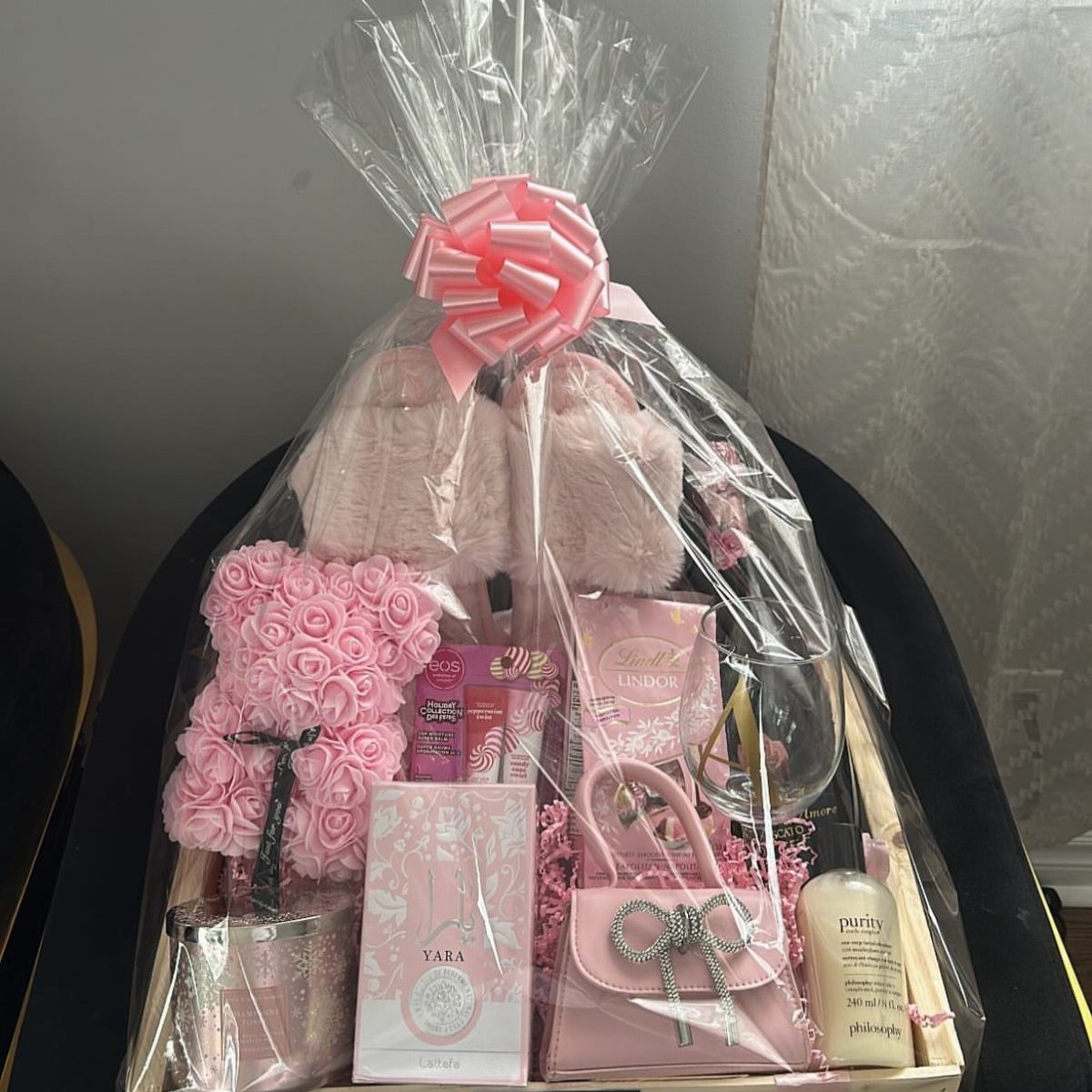 14 Household Gift Basket Ideas for Every Occasion 12 Pink gift basket with fluffy slippers, rose teddy bear, and beauty products wrapped in cellophane.