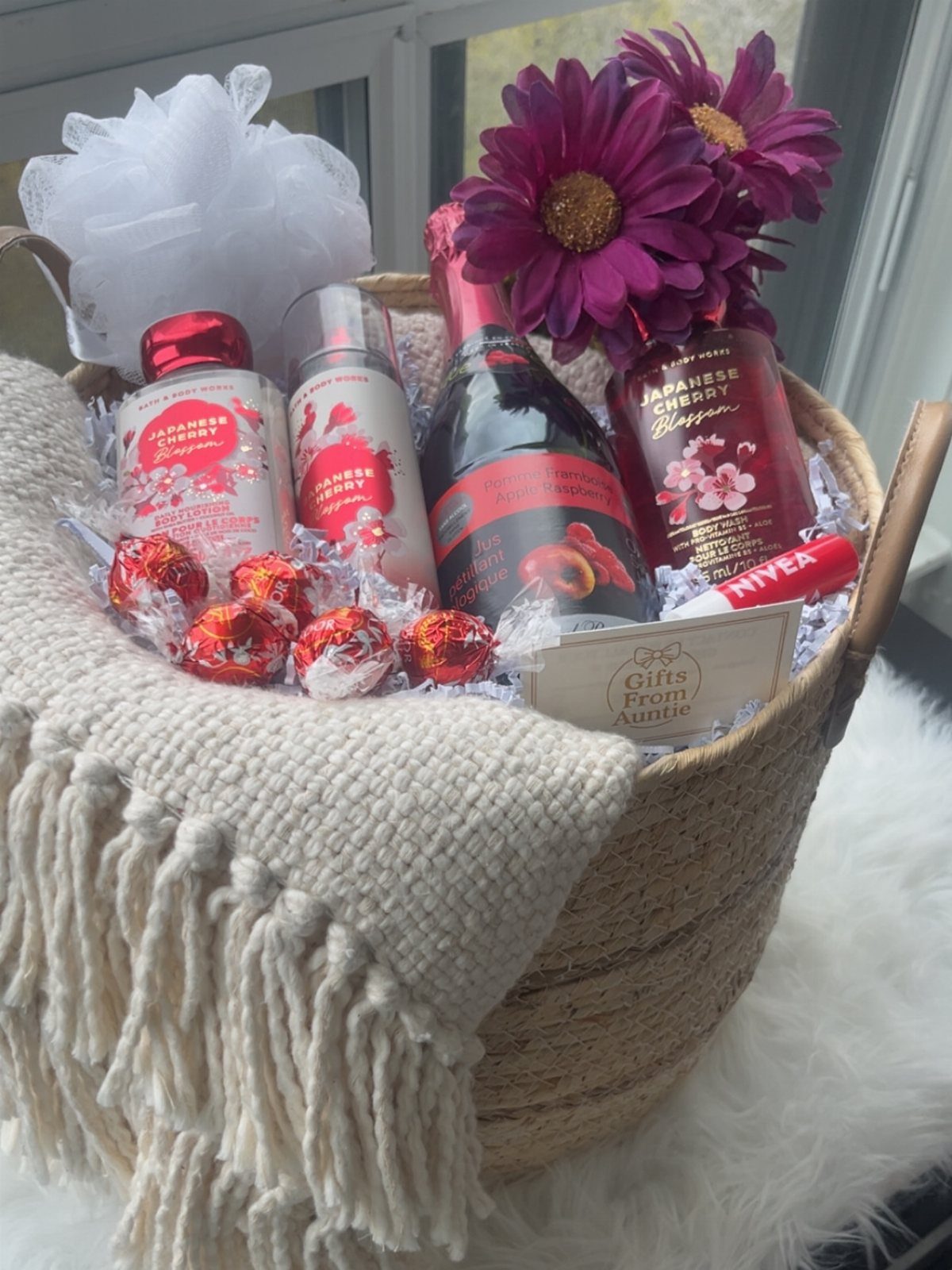 14 Household Gift Basket Ideas for Every Occasion 4 Wicker gift basket with scented lotions, sparkling wine, chocolates, and a cream blanket.