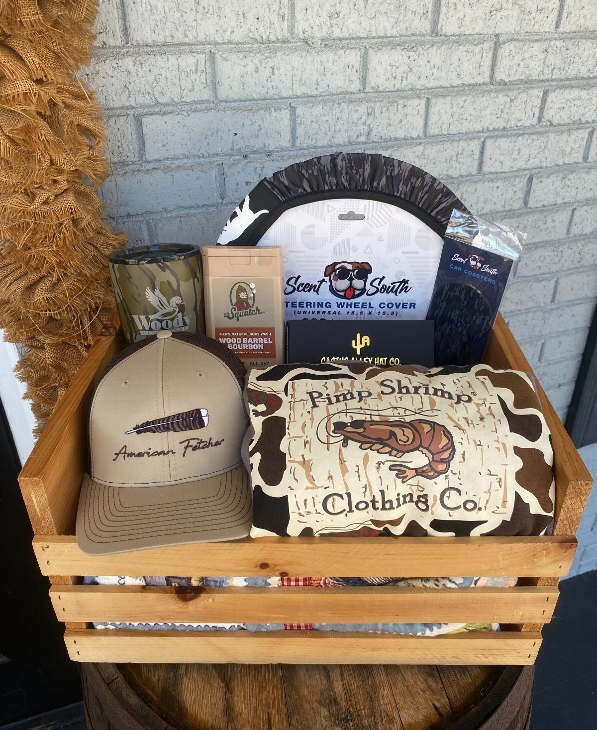 Hunting Gift Basket Ideas: 7 Options to Give This Year 5 Wooden gift crate containing a tan cap, shrimp patterned cloth, and camouflage cup.