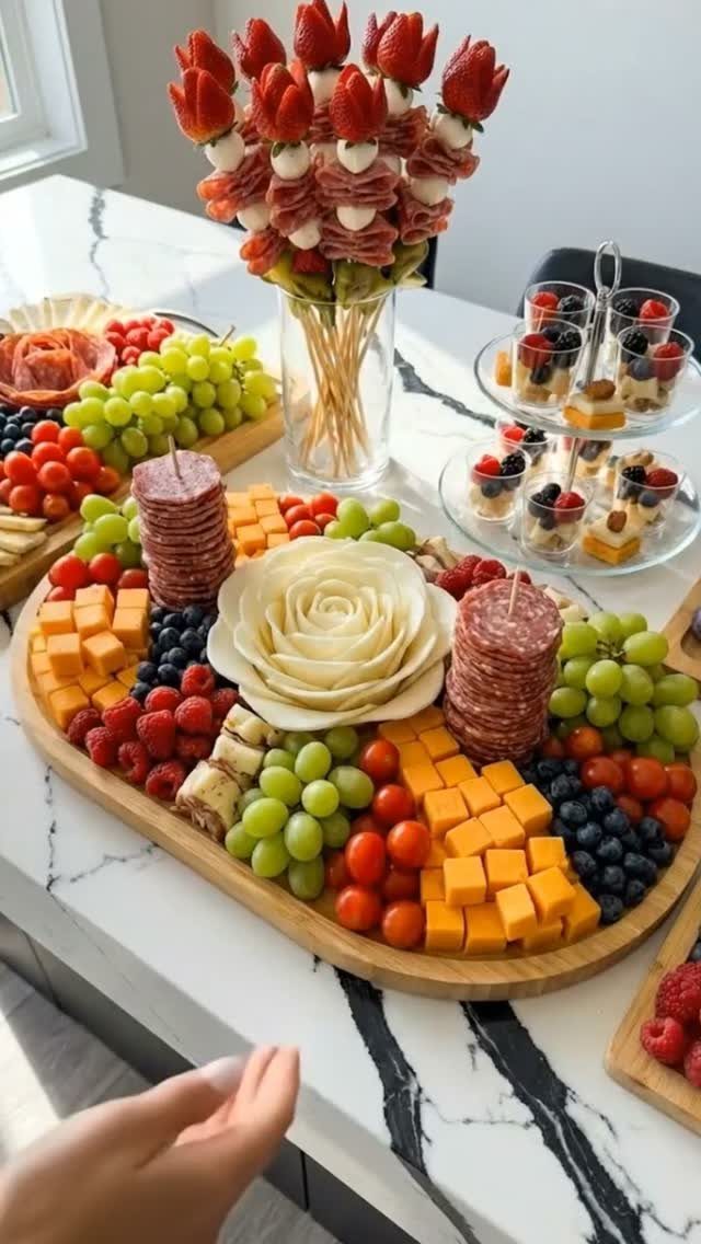 Wooden charcuterie board with cheese, salami, grapes, and berries on a marble counter.