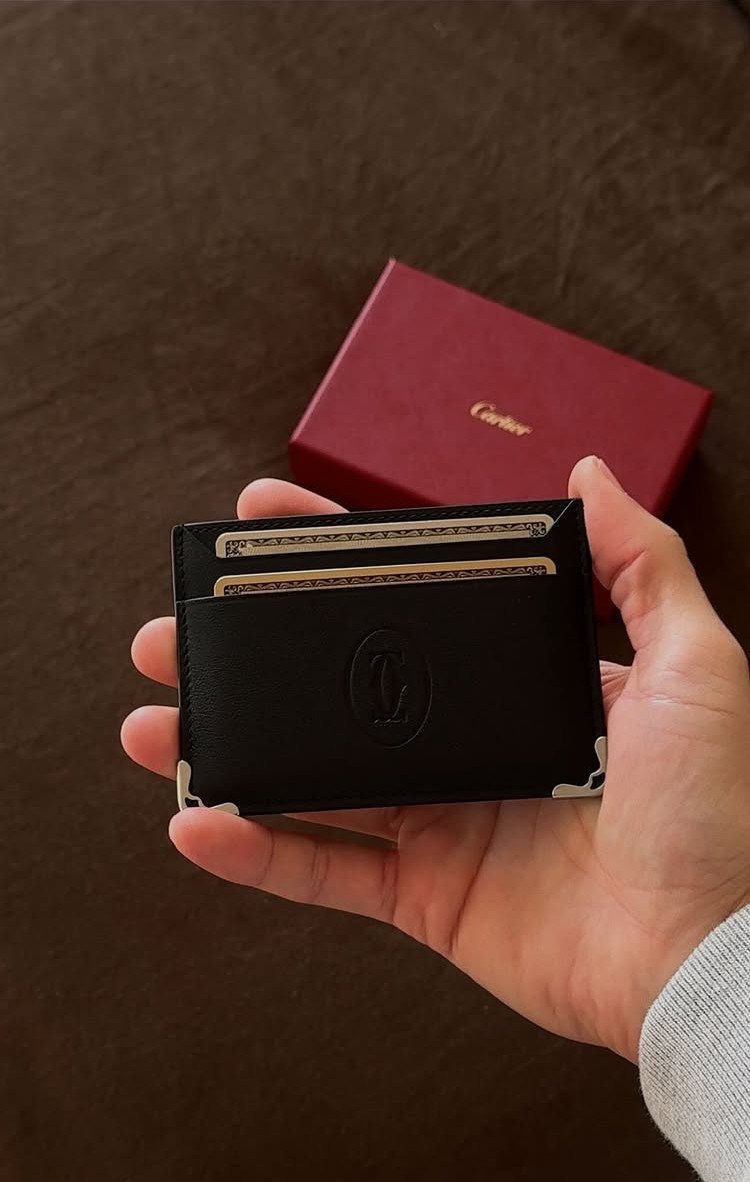 Black leather Cartier card holder held in hand with red gift box background
