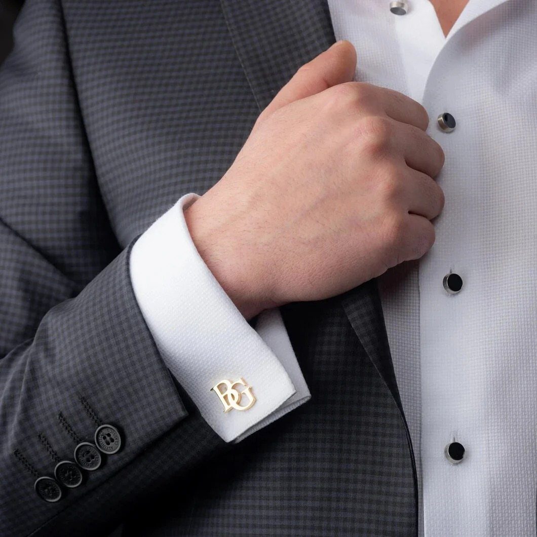 Gold monogrammed cufflink with letters BG on a white shirt cuff and grey suit.