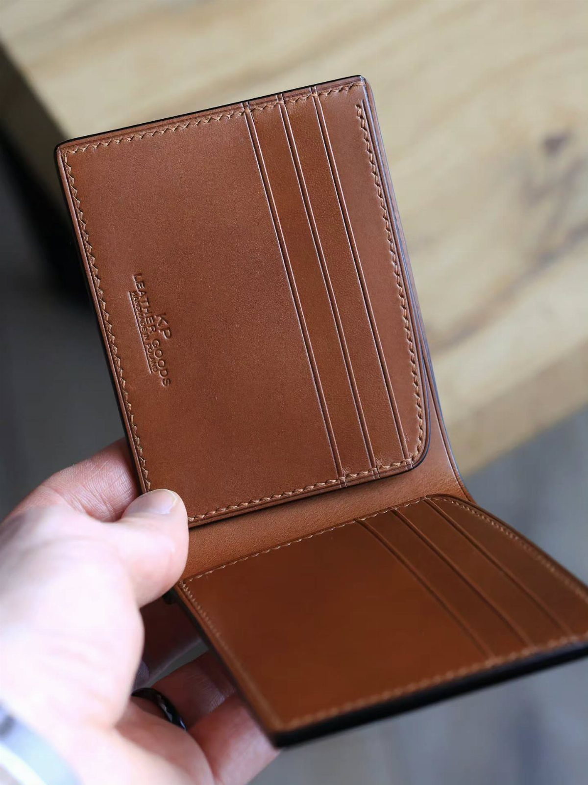 Brown leather bi-fold wallet held open by a hand against a wooden background