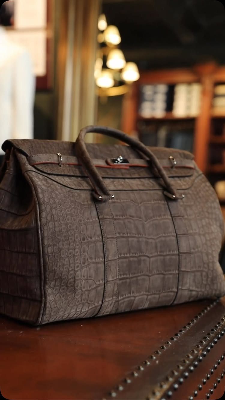 Brown crocodile-embossed leather weekend bag resting on a polished wooden table.