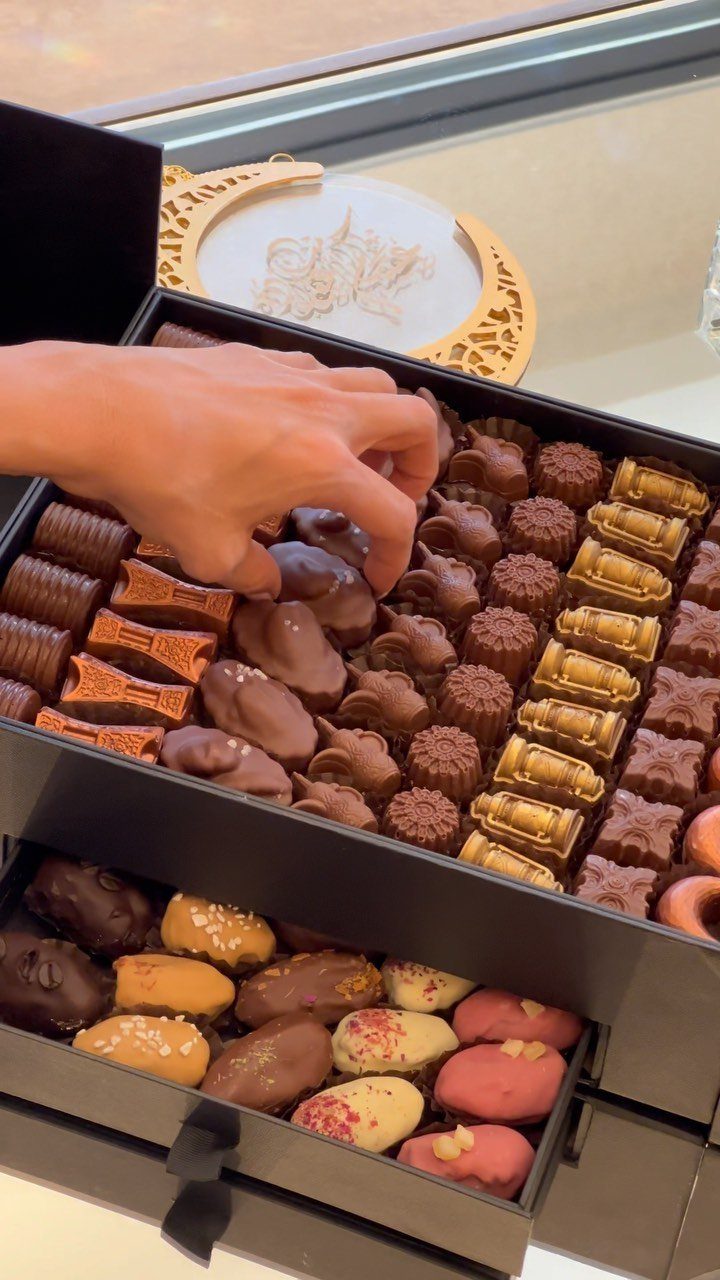 Assorted gourmet chocolates in a black tiered gift box with a hand reaching in.