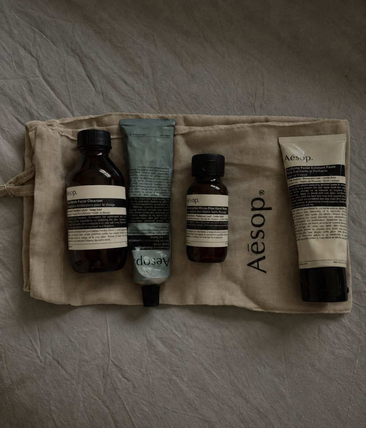 Aesop skincare bottles and tubes resting on a beige fabric toiletry pouch.
