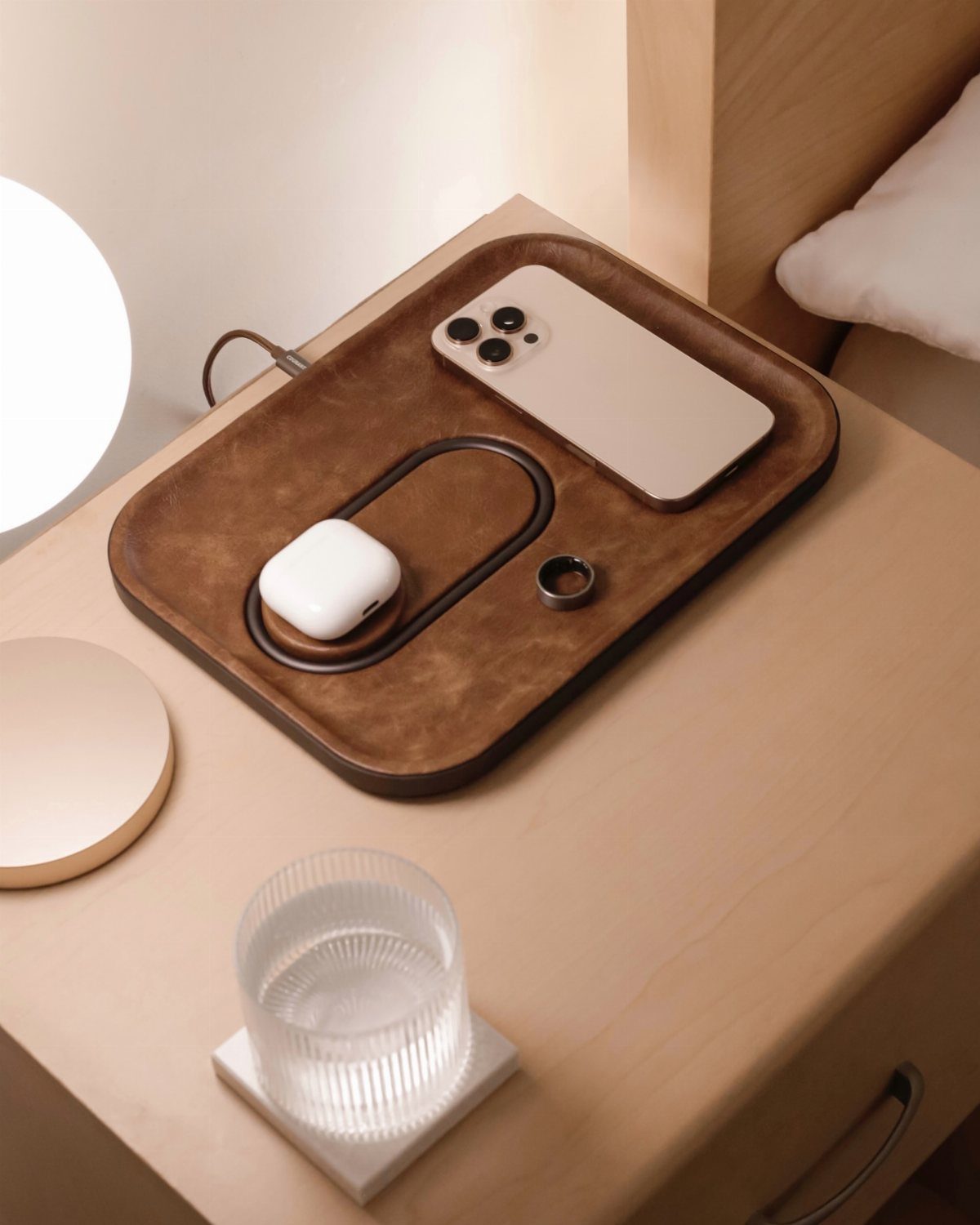Brown leather valet tray with smartphone, earbuds, and ring on wooden nightstand
