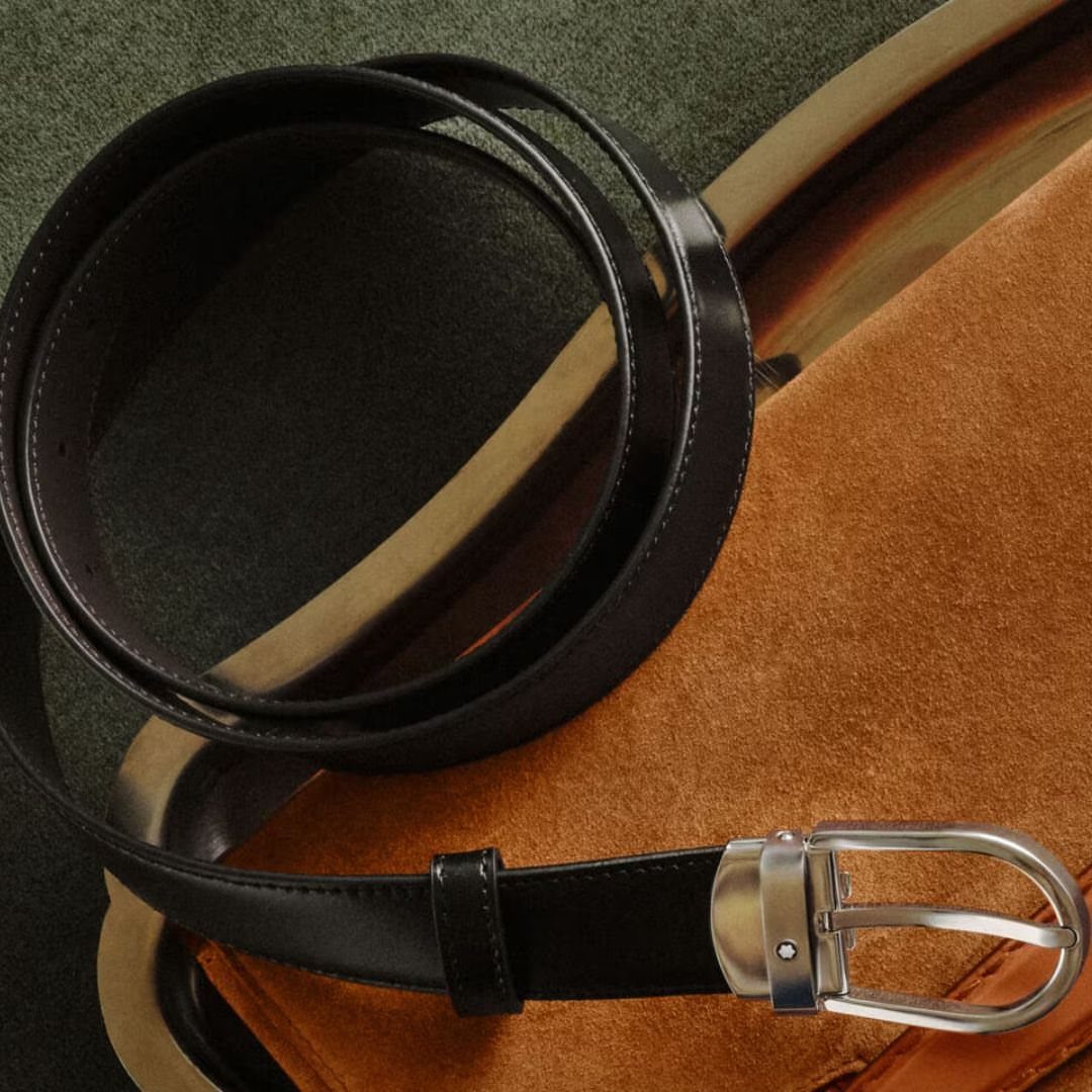 Black leather belt with silver buckle on brown suede and green fabric.