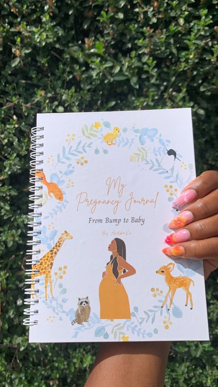 Pregnancy journal with animal illustrations held by a hand against green foliage.