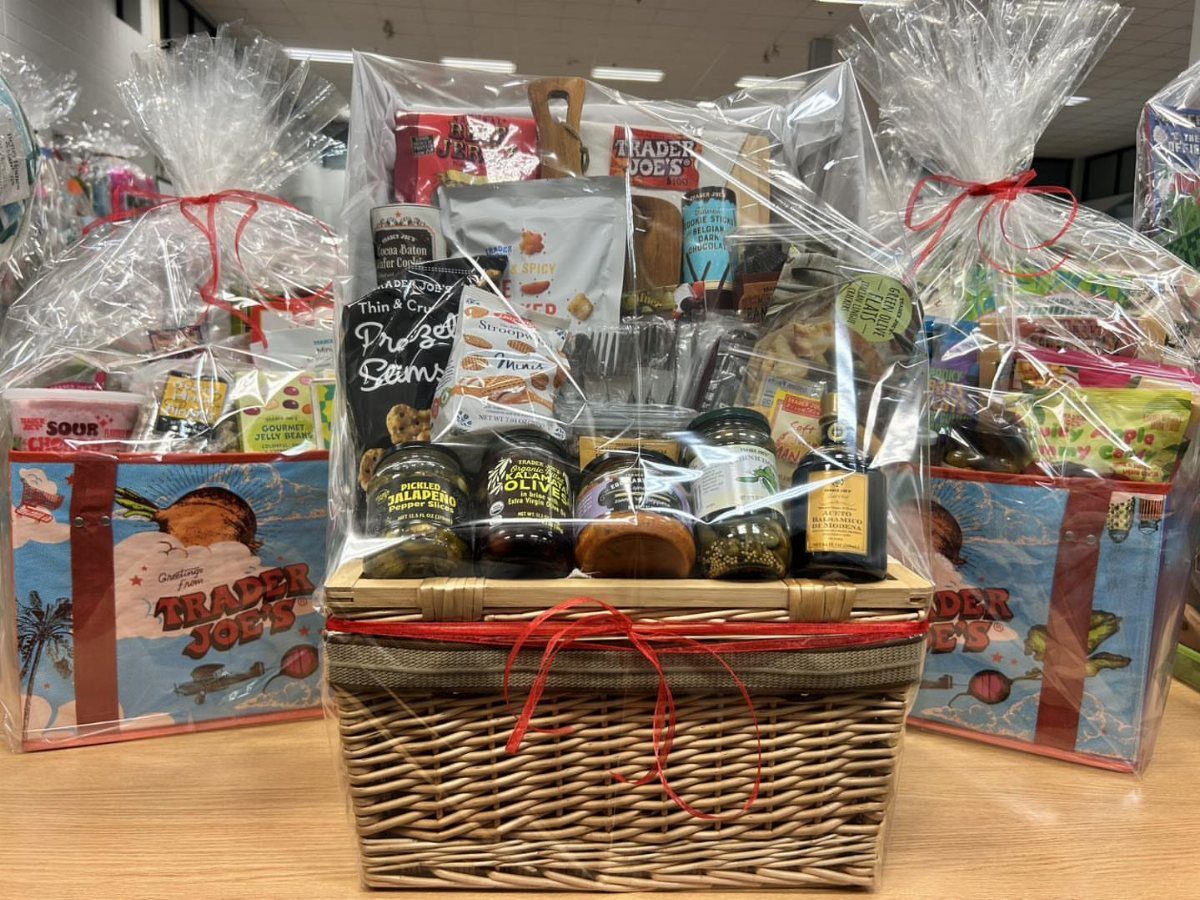 Three cellophane-wrapped gift baskets filled with gourmet snacks and jars on a table.